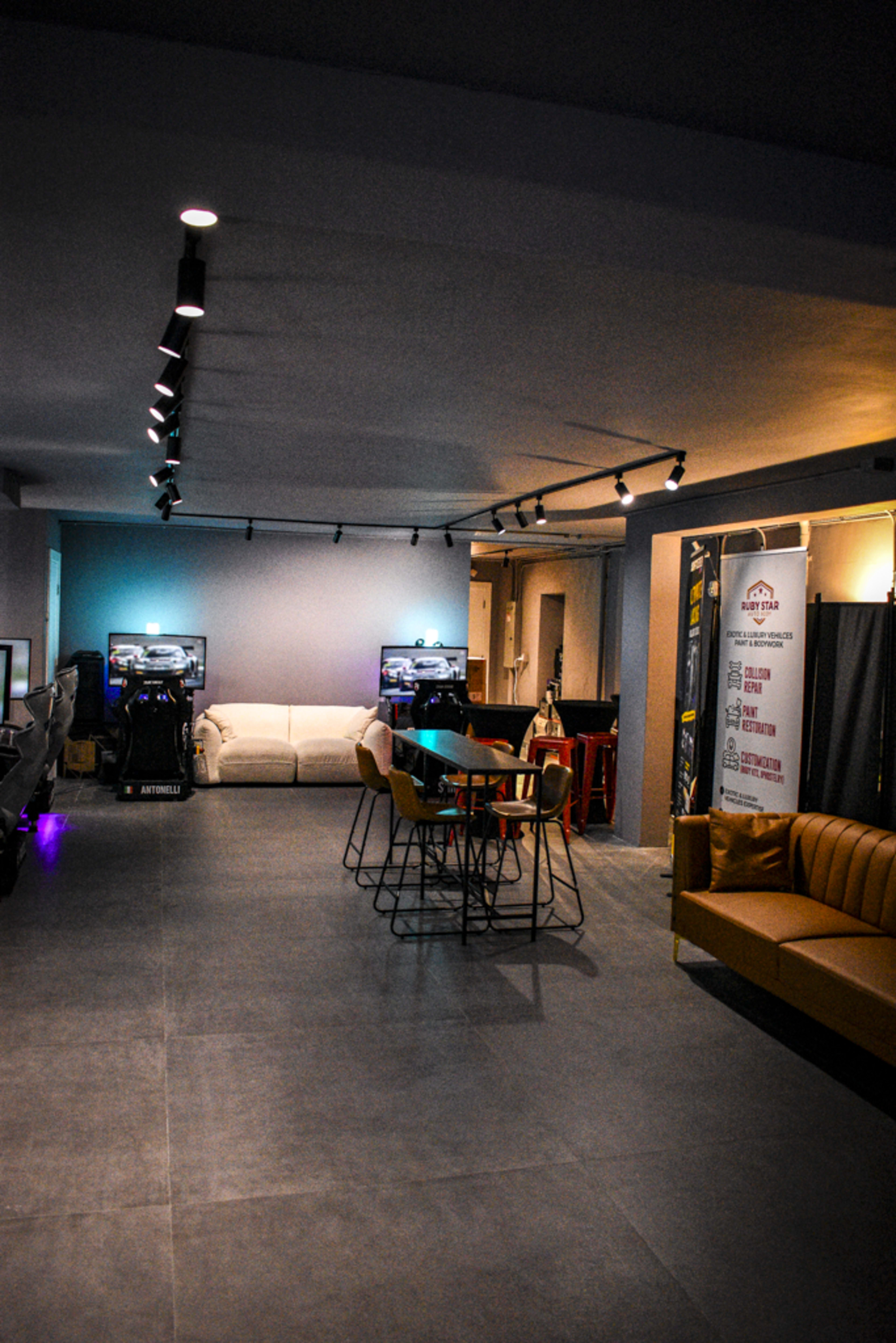 The image shows a modern lounge area with multiple seating options, including couches and bar stools, and arcade machines in the background.