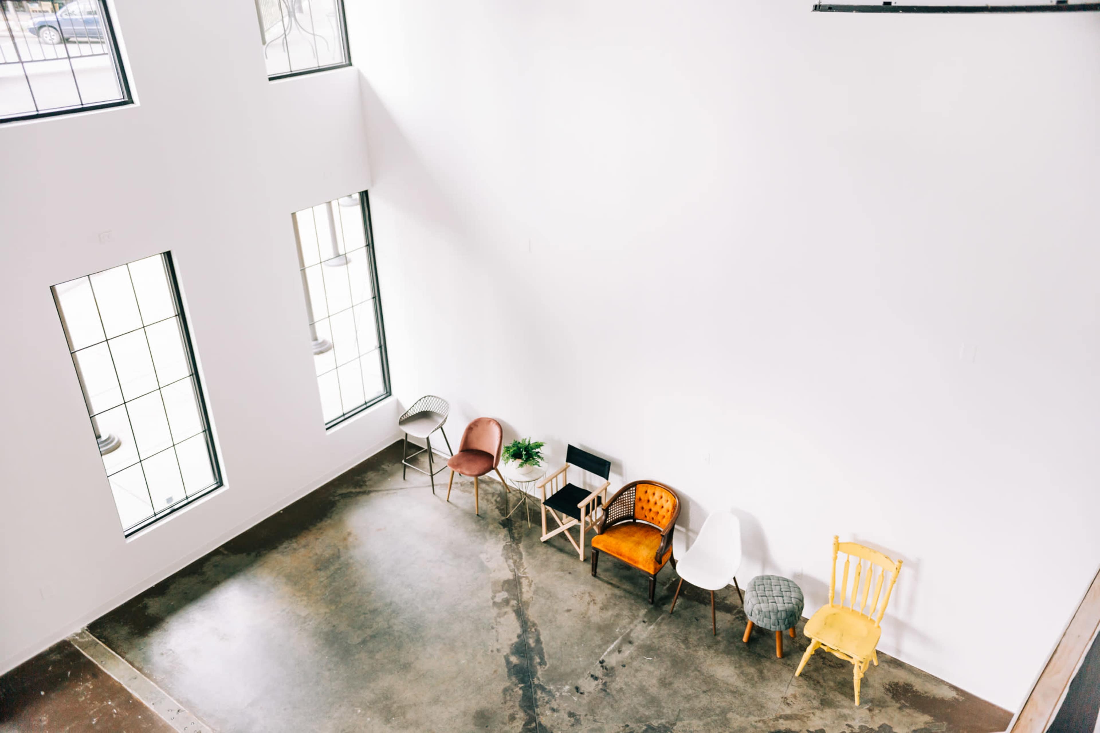 A spacious, well-lit room with a polished concrete floor and several chairs arranged along a white wall beneath large windows.