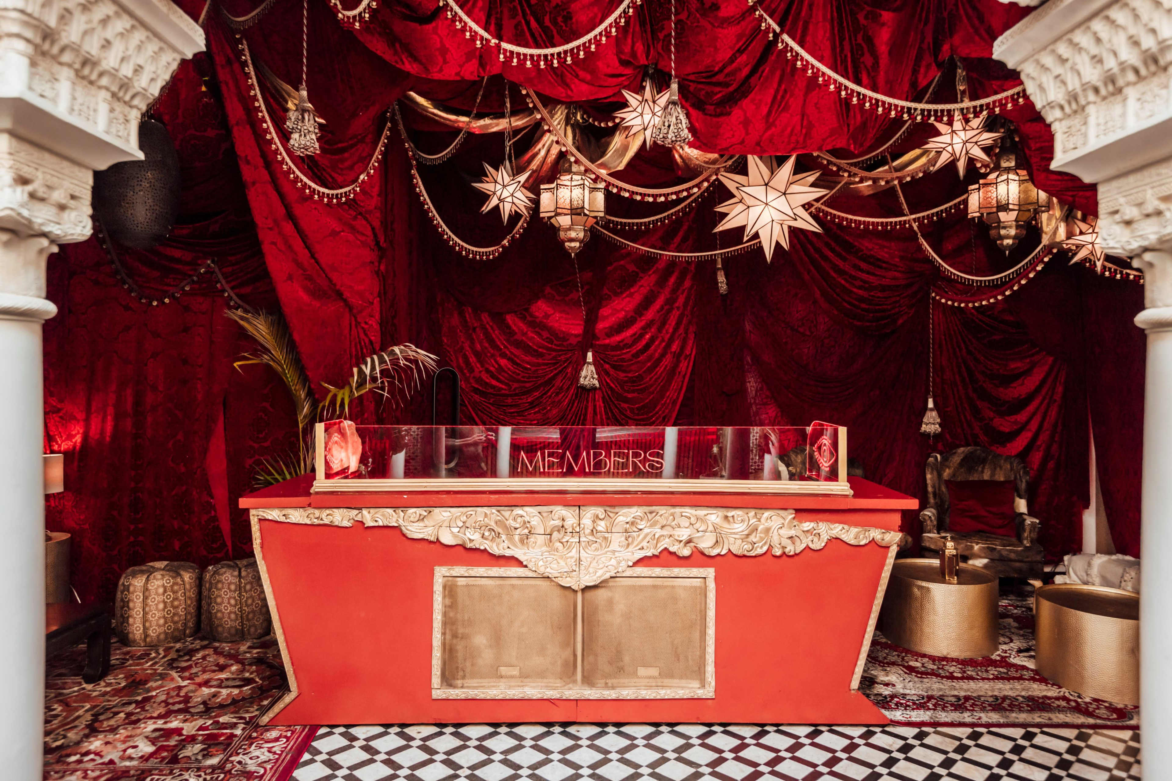 An elaborately decorated reception area with red draped fabric, ornate lanterns, and a red and gold counter labeled "MEMBERS."