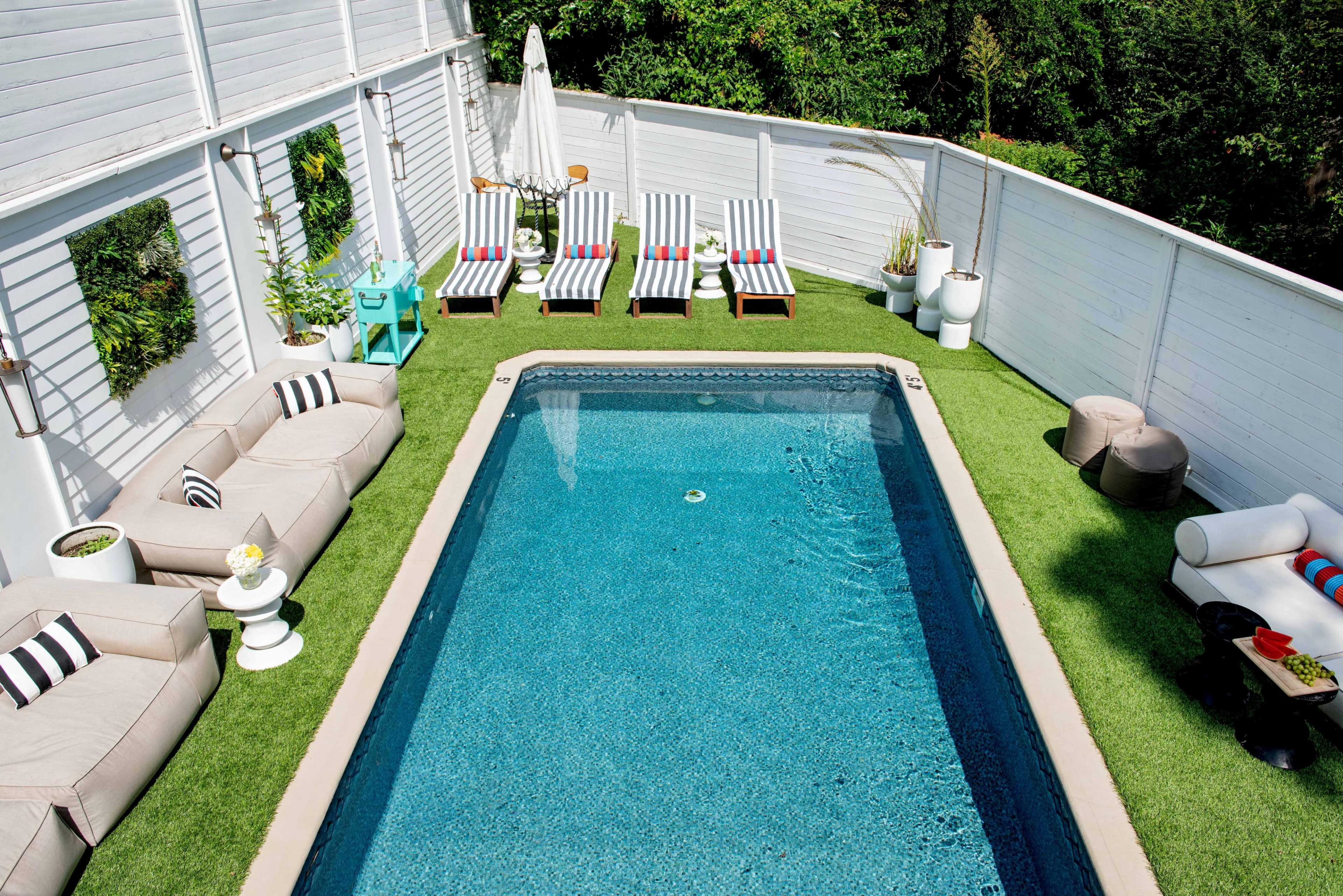 A backyard swimming pool surrounded by two sets of lounge chairs and outdoor seating on a grass-like surface.