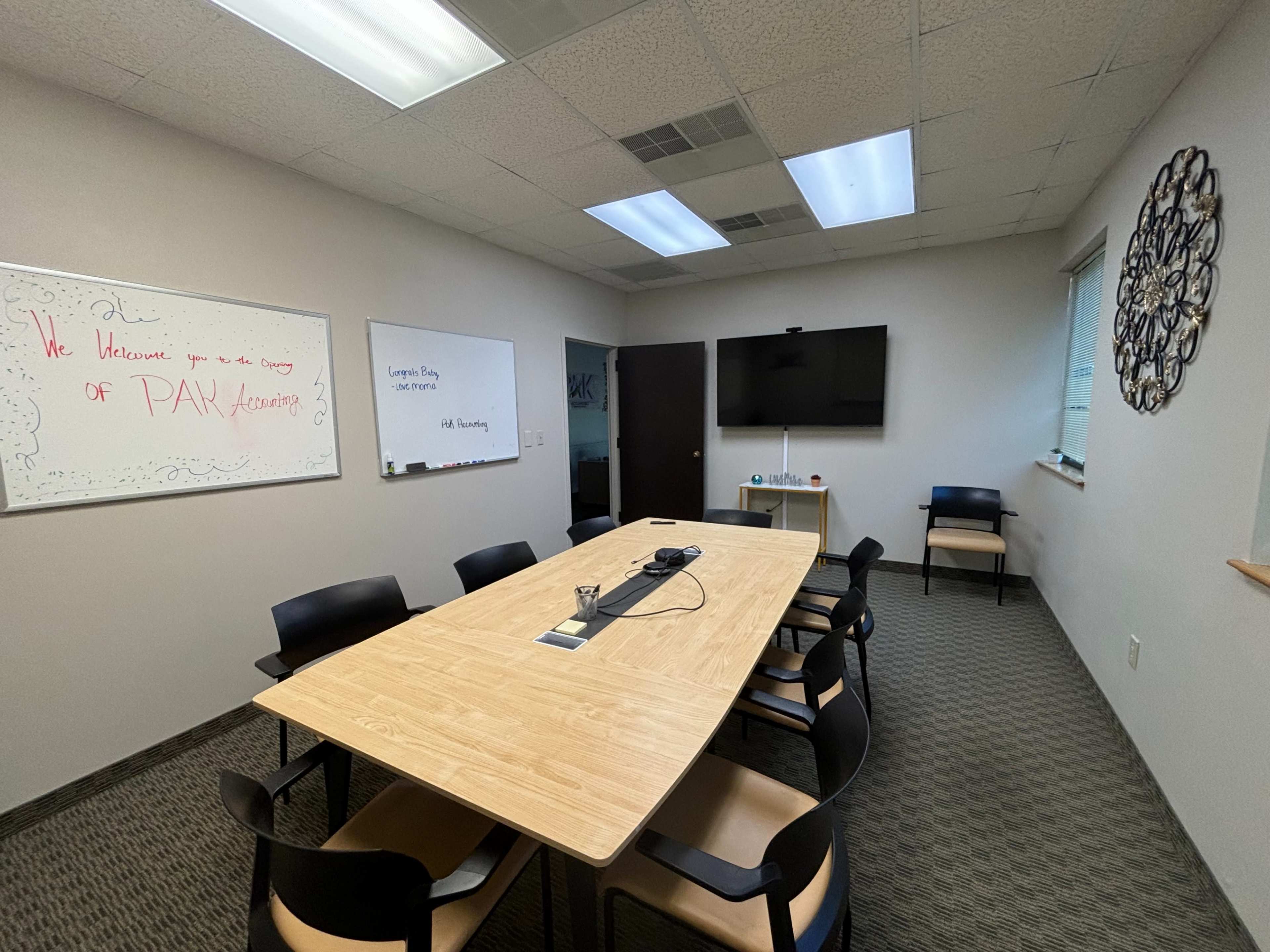 The image shows a conference room with a large rectangular table surrounded by chairs, whiteboards on the walls, and a wall-mounted television.