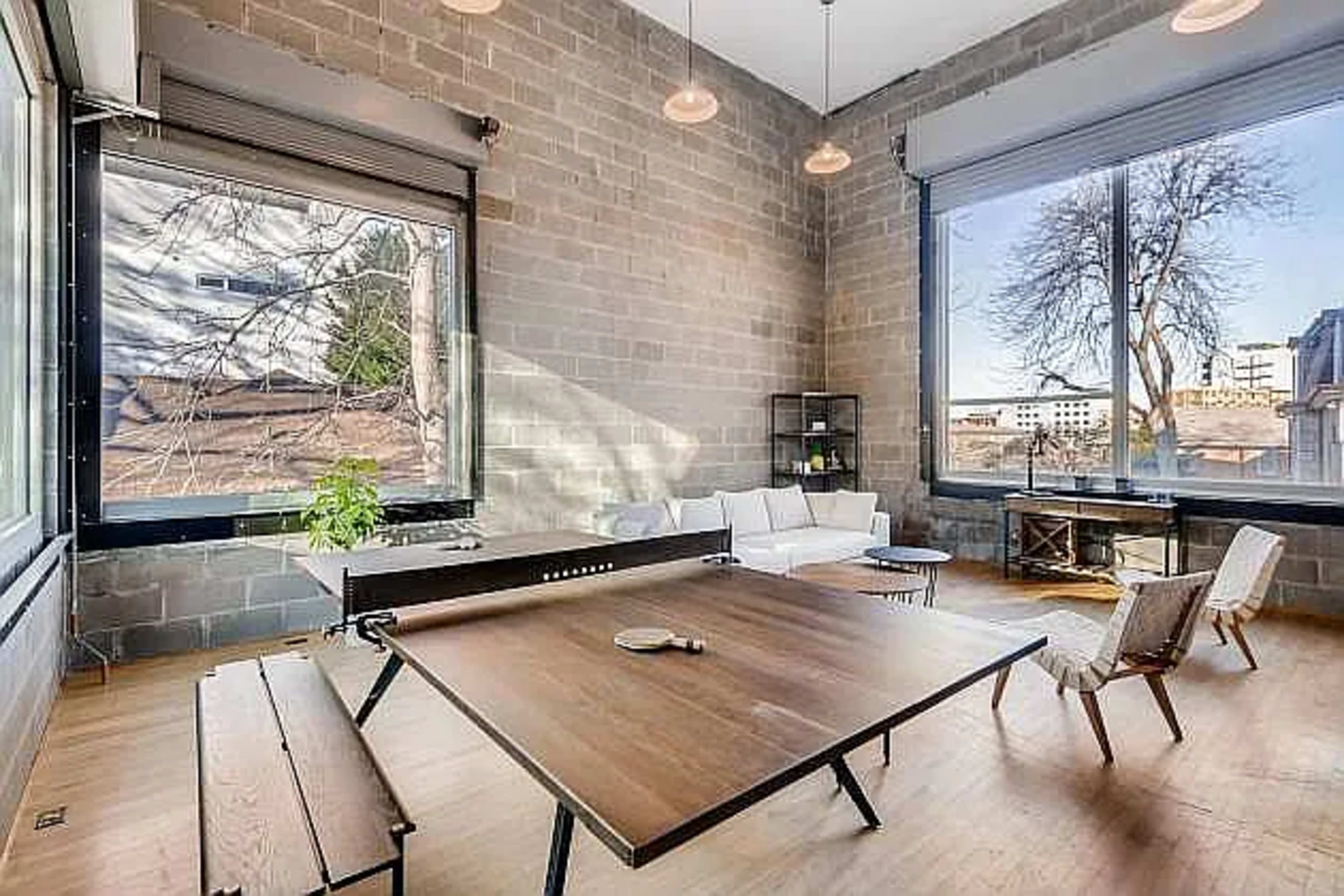 A modern, minimalist room with large windows, a wooden table at the center, and a sectional sofa against the wall.