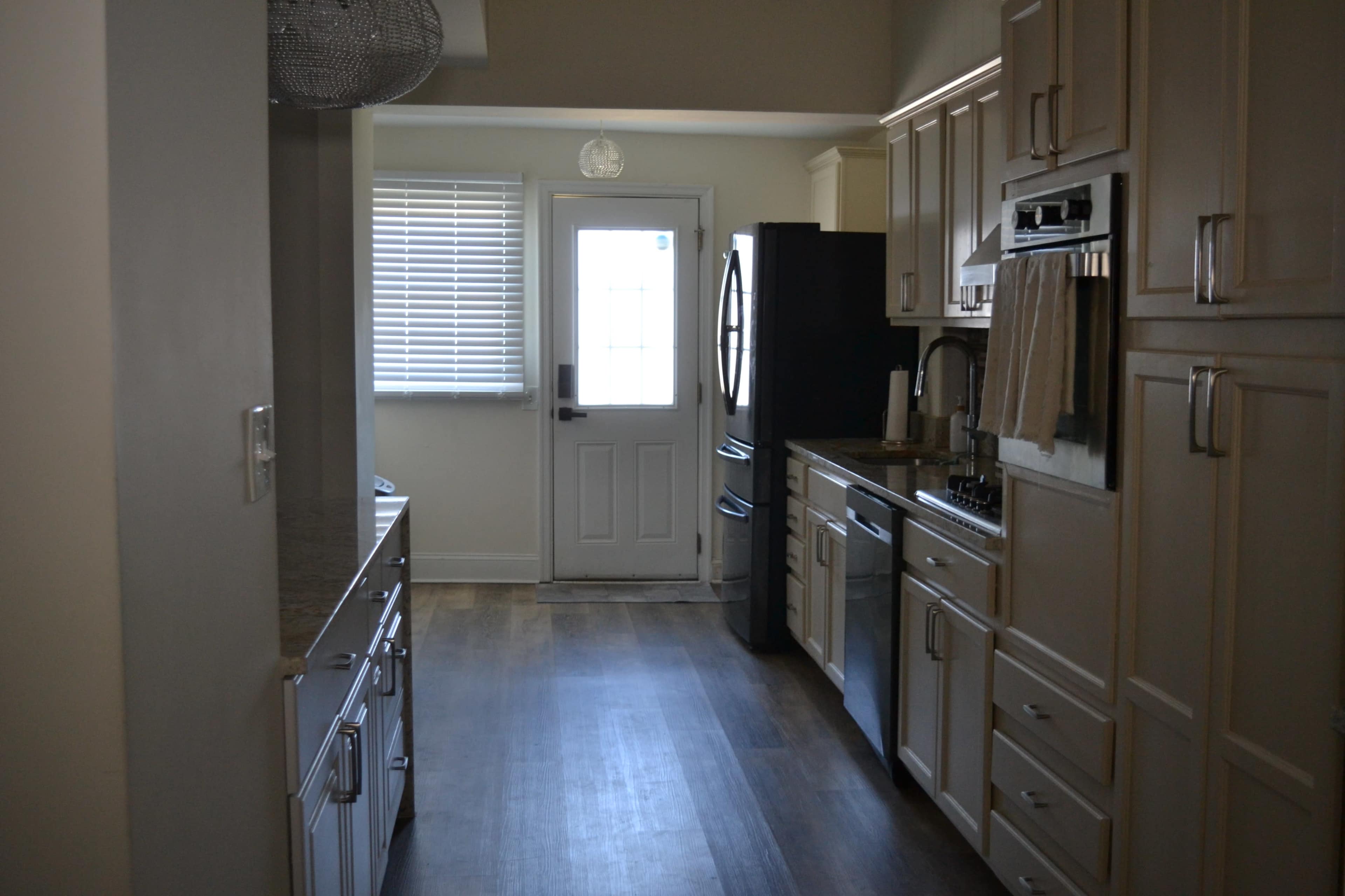The image shows a modern kitchen featuring light-colored cabinetry, stainless steel appliances, and a door leading outside, with natural light coming through a window.
