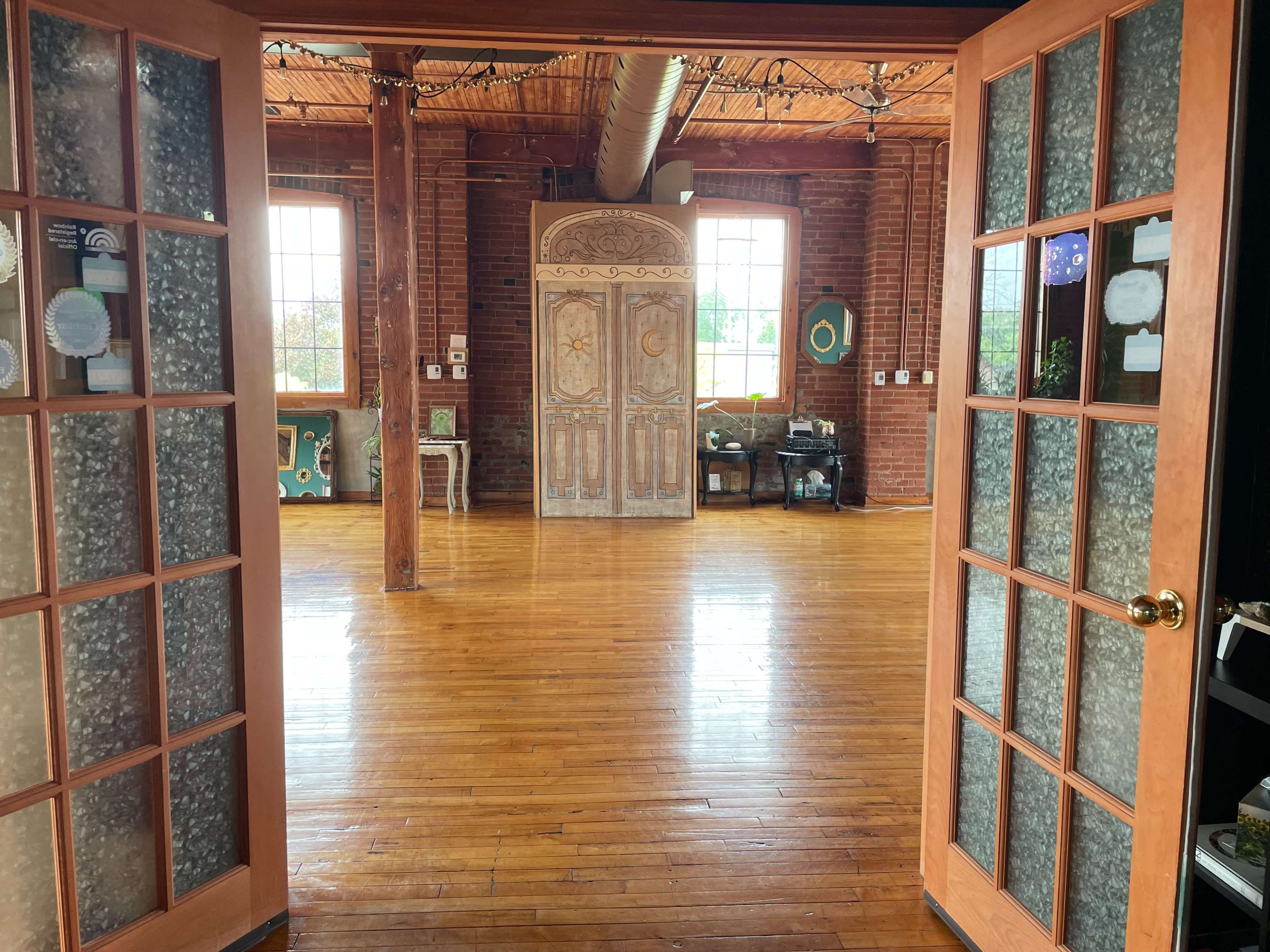 The image shows a spacious interior with wooden floors and large windows, viewed through a set of glass double doors.