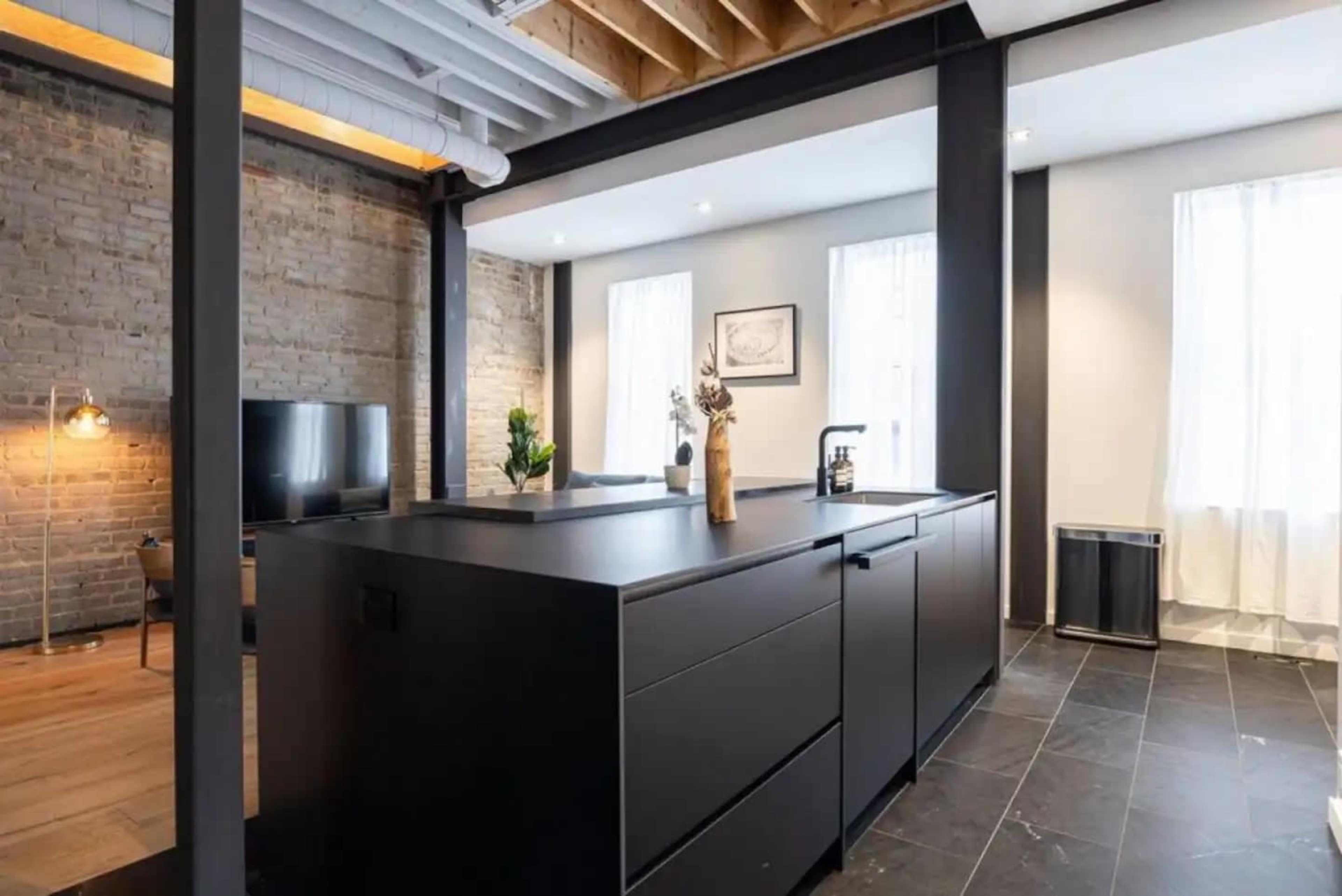 A modern kitchen with a large black island, stone walls, and large windows that let in natural light.