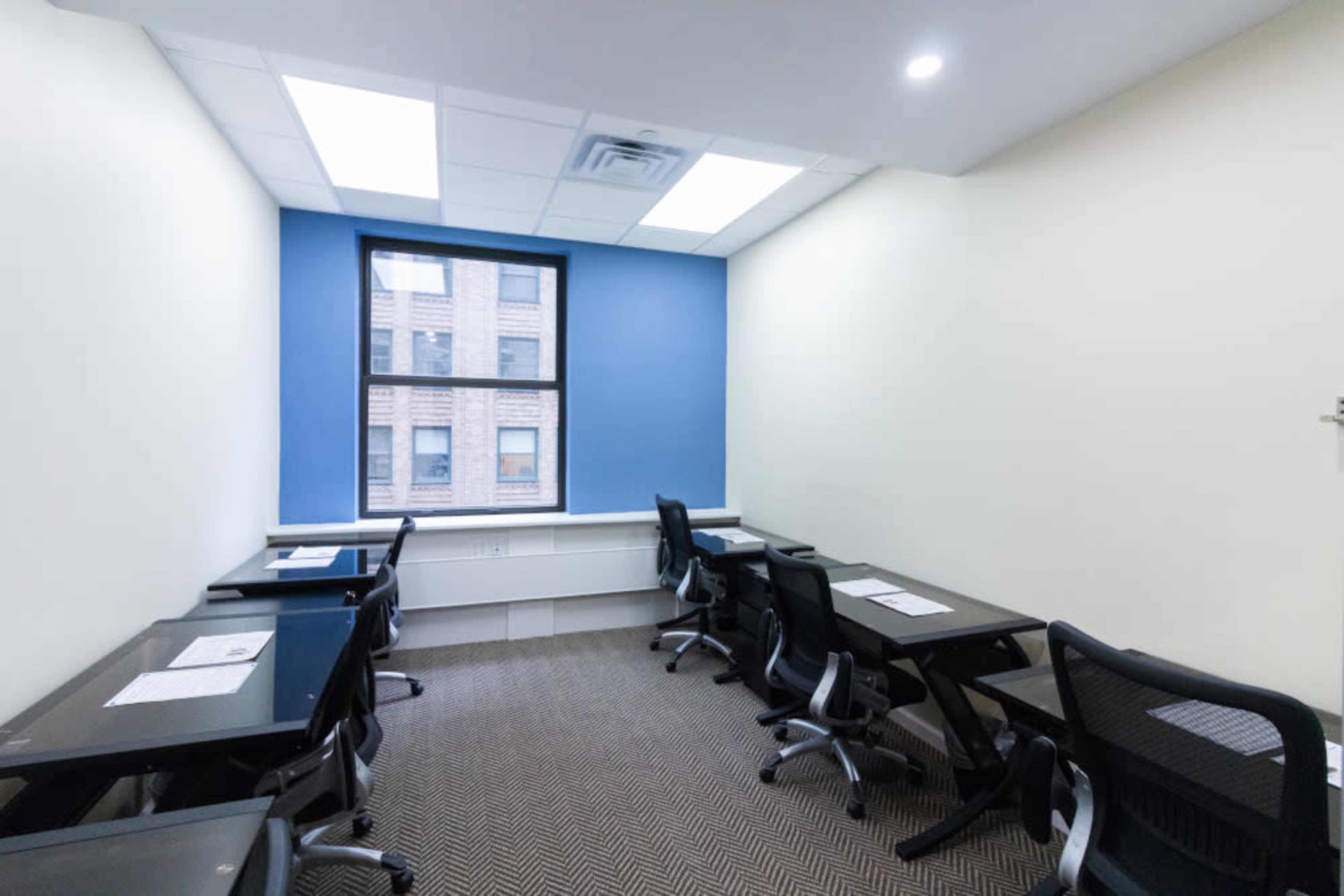 A small meeting room with several black chairs and desks arranged around a window with blue walls.