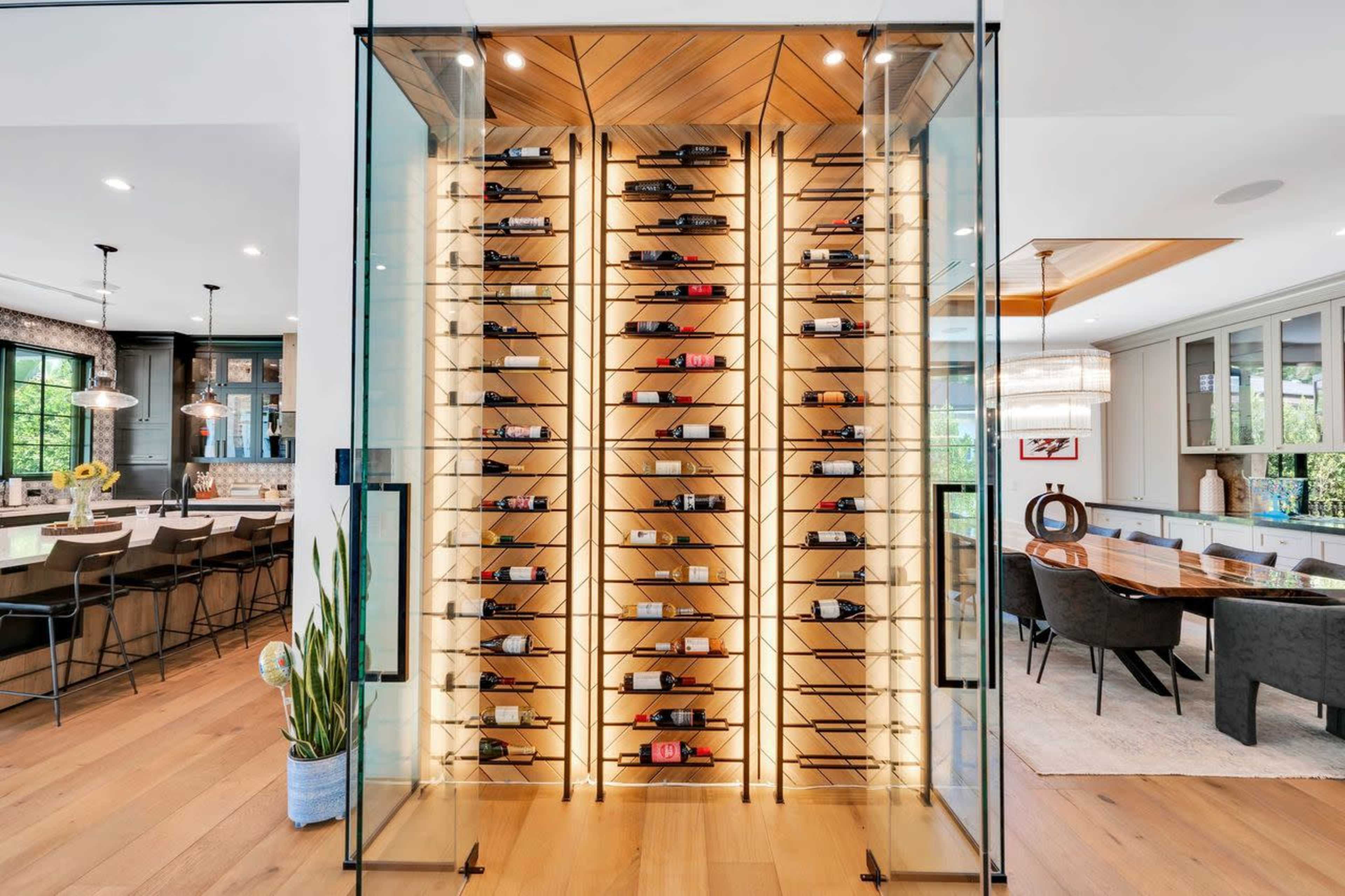 The image features a wine display consisting of numerous bottles arranged on vertical racks illuminated by soft lighting, set within a glass-enclosed area.