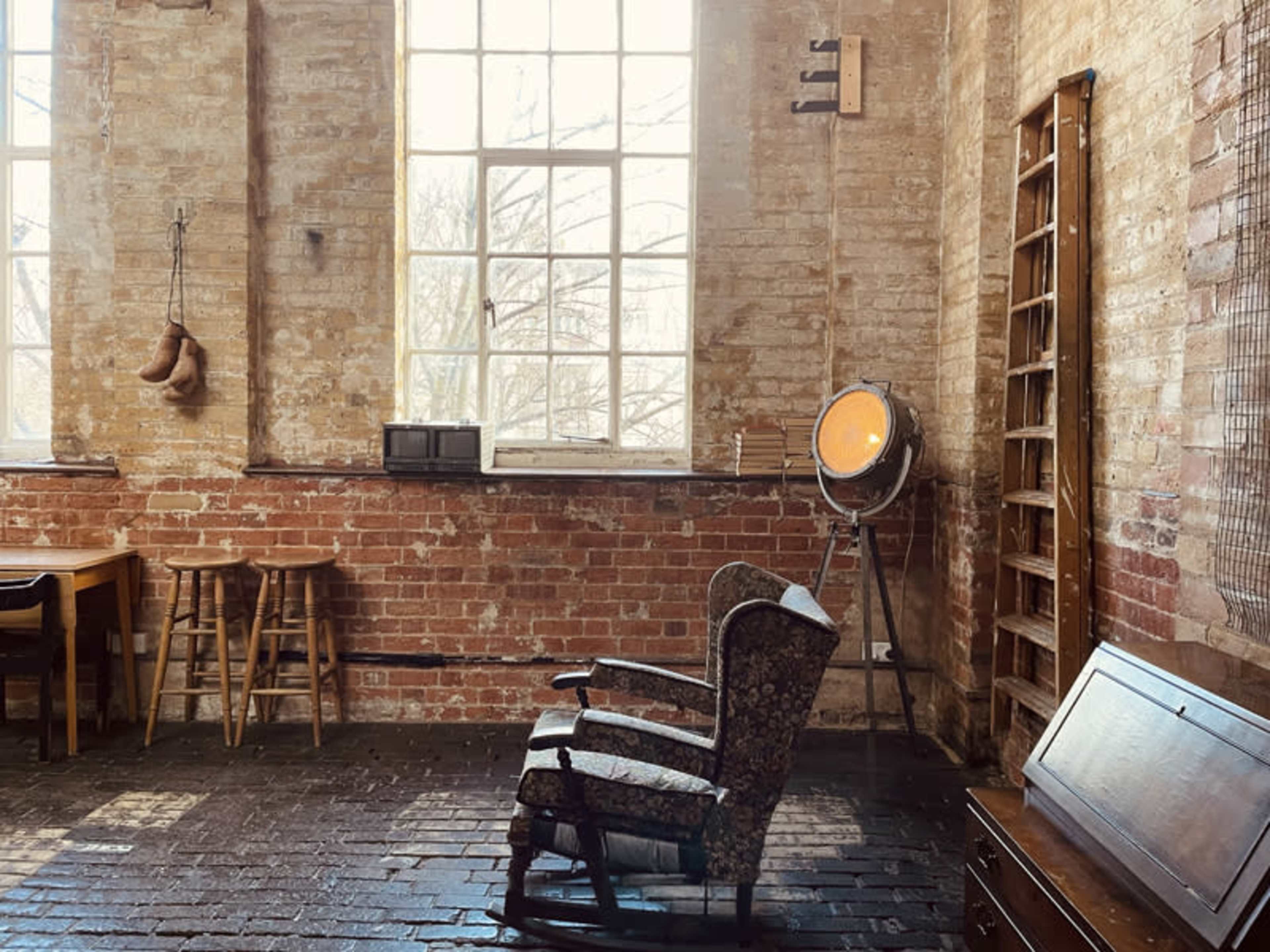 A rustic interior space with exposed brick walls, a vintage rocking chair, a spotlight, and wooden furniture.