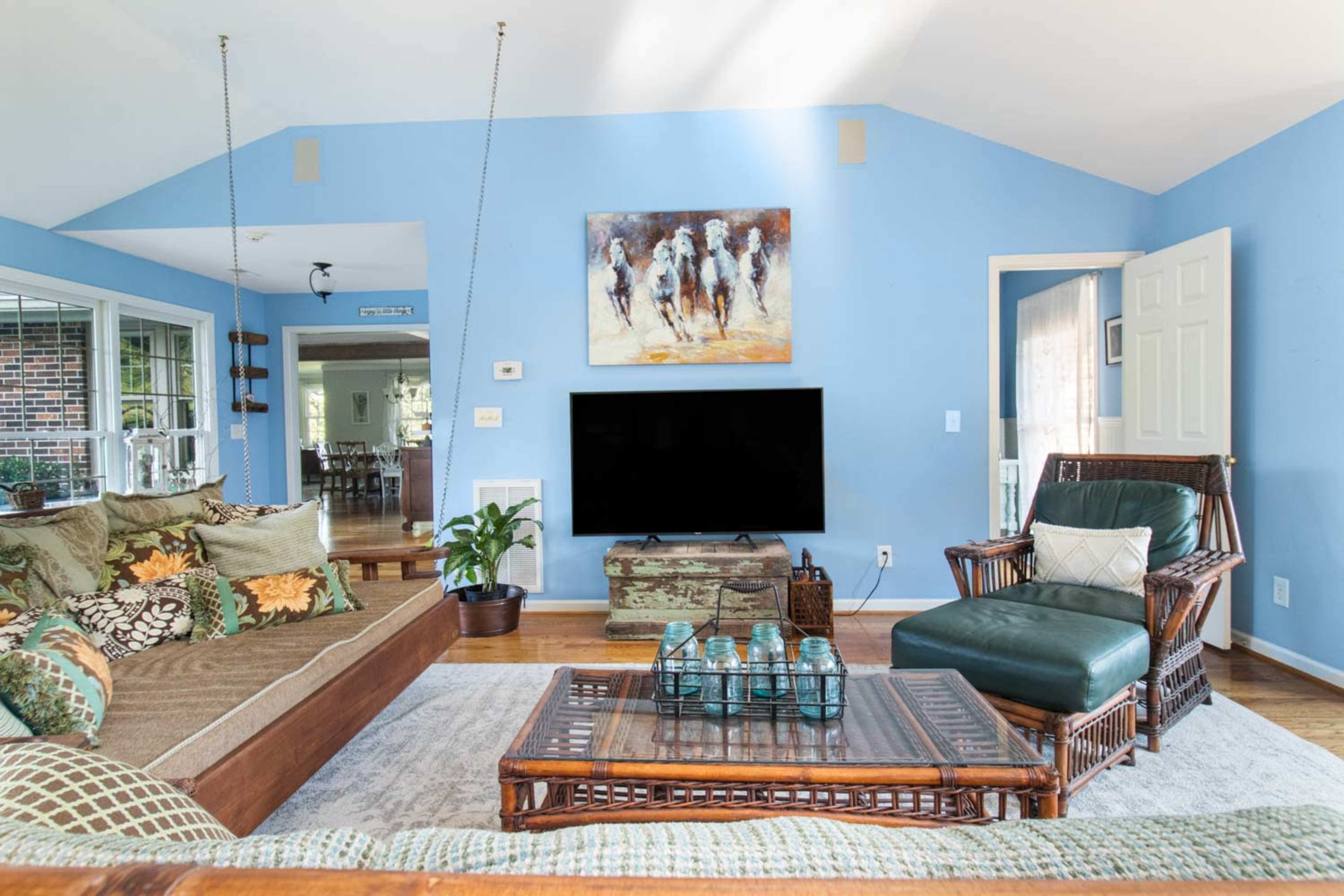 A spacious living room featuring a blue wall, a large flat-screen TV, a wooden coffee table, and a mix of comfortable seating options.