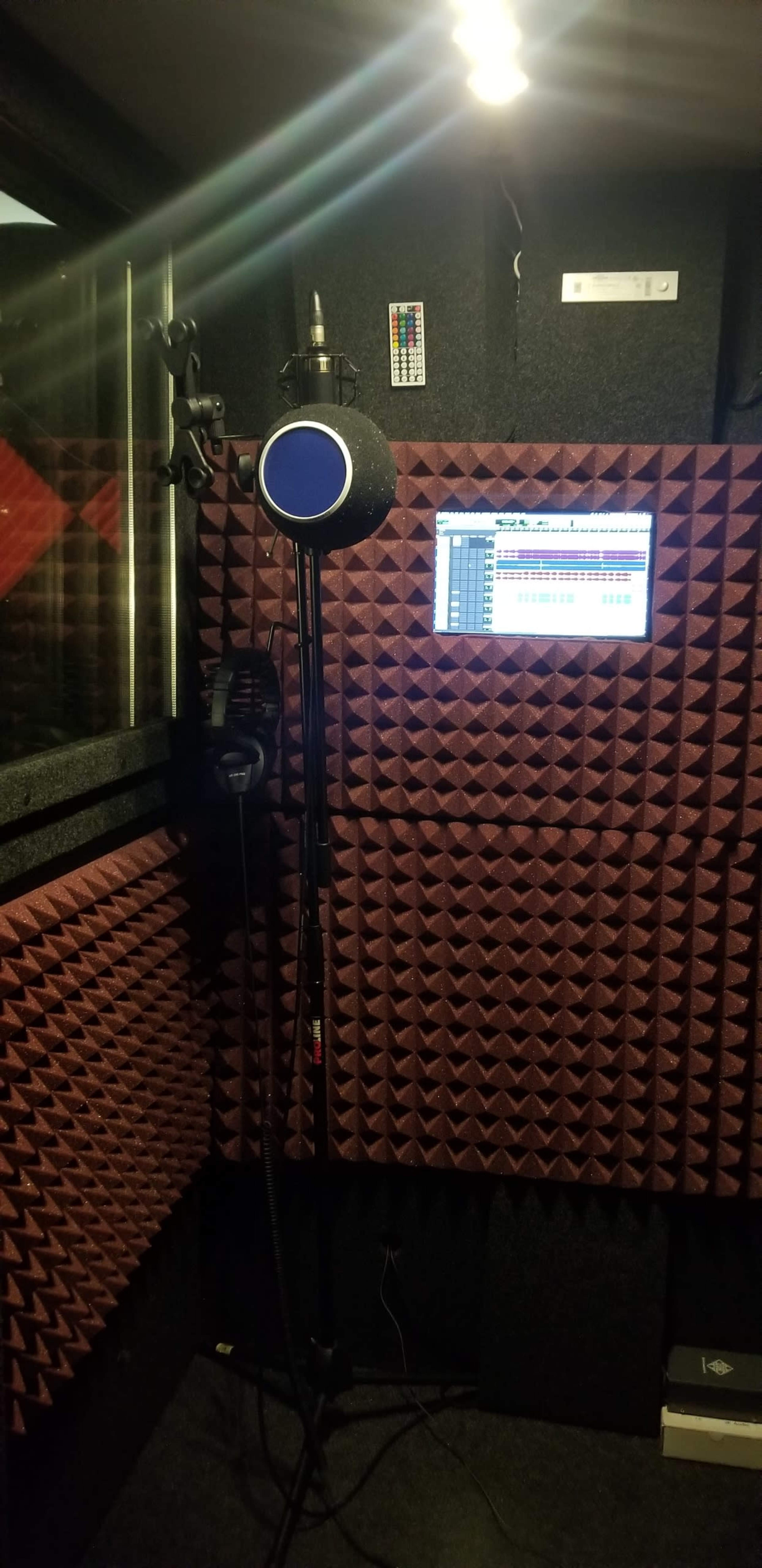 A soundproof recording booth equipped with a microphone, a mic stand, and a digital display for audio recording.