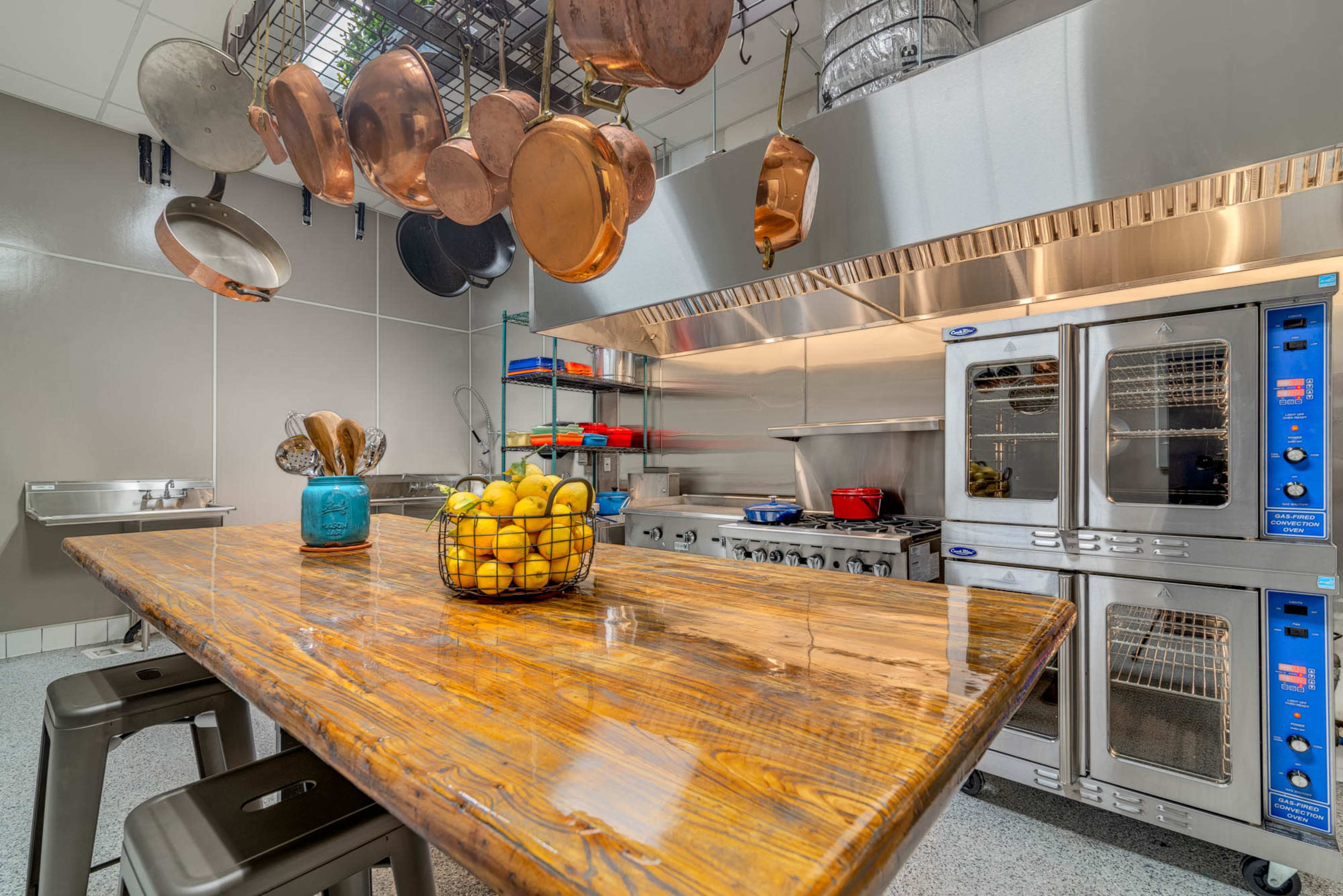 A well-equipped kitchen featuring a large wooden table, hanging pots, and stainless steel appliances.