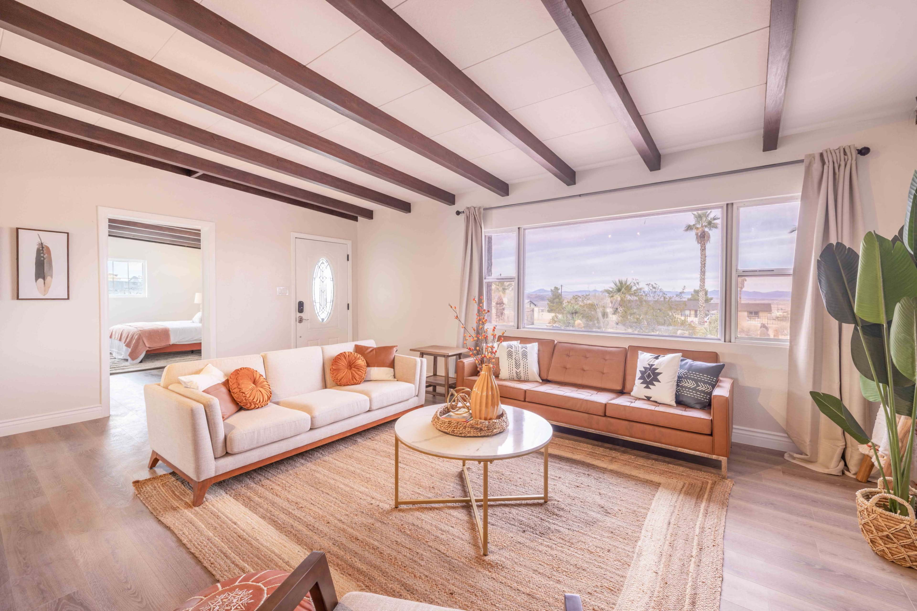 The scene shows a living room with a mix of modern and classic furniture, featuring a large window offering a view of palm trees outside.