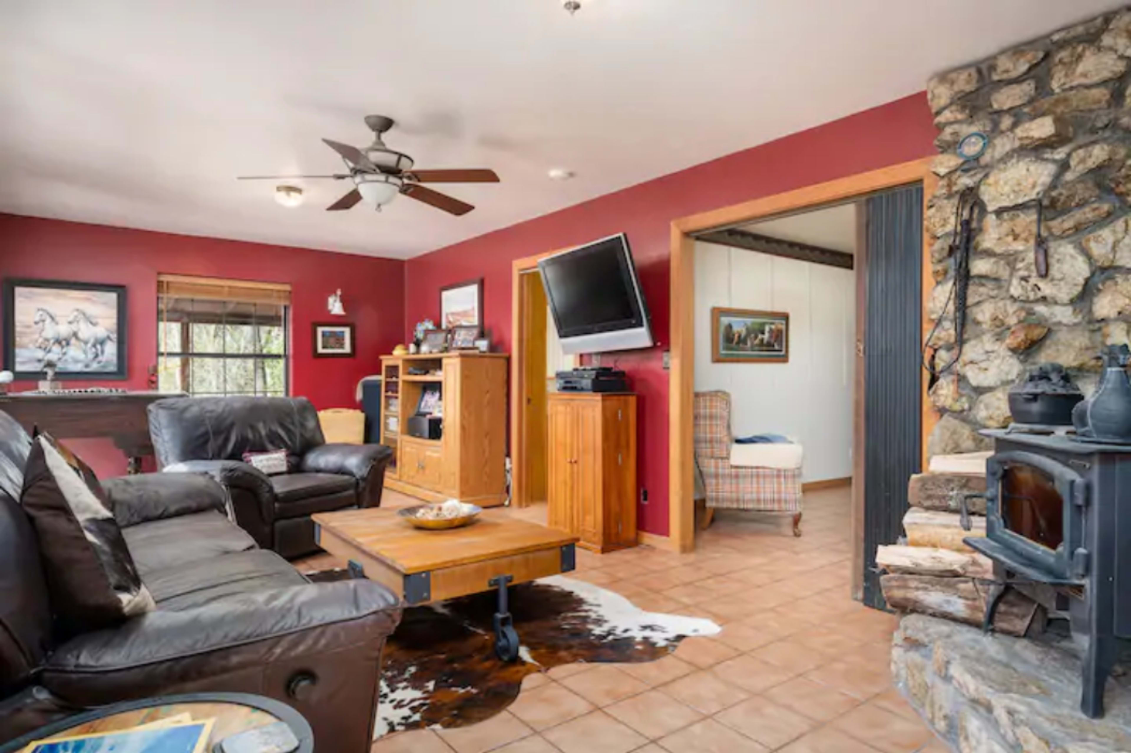 The living room features leather sofas, a wooden coffee table on a tiled floor, a stone fireplace, and a wall-mounted television.