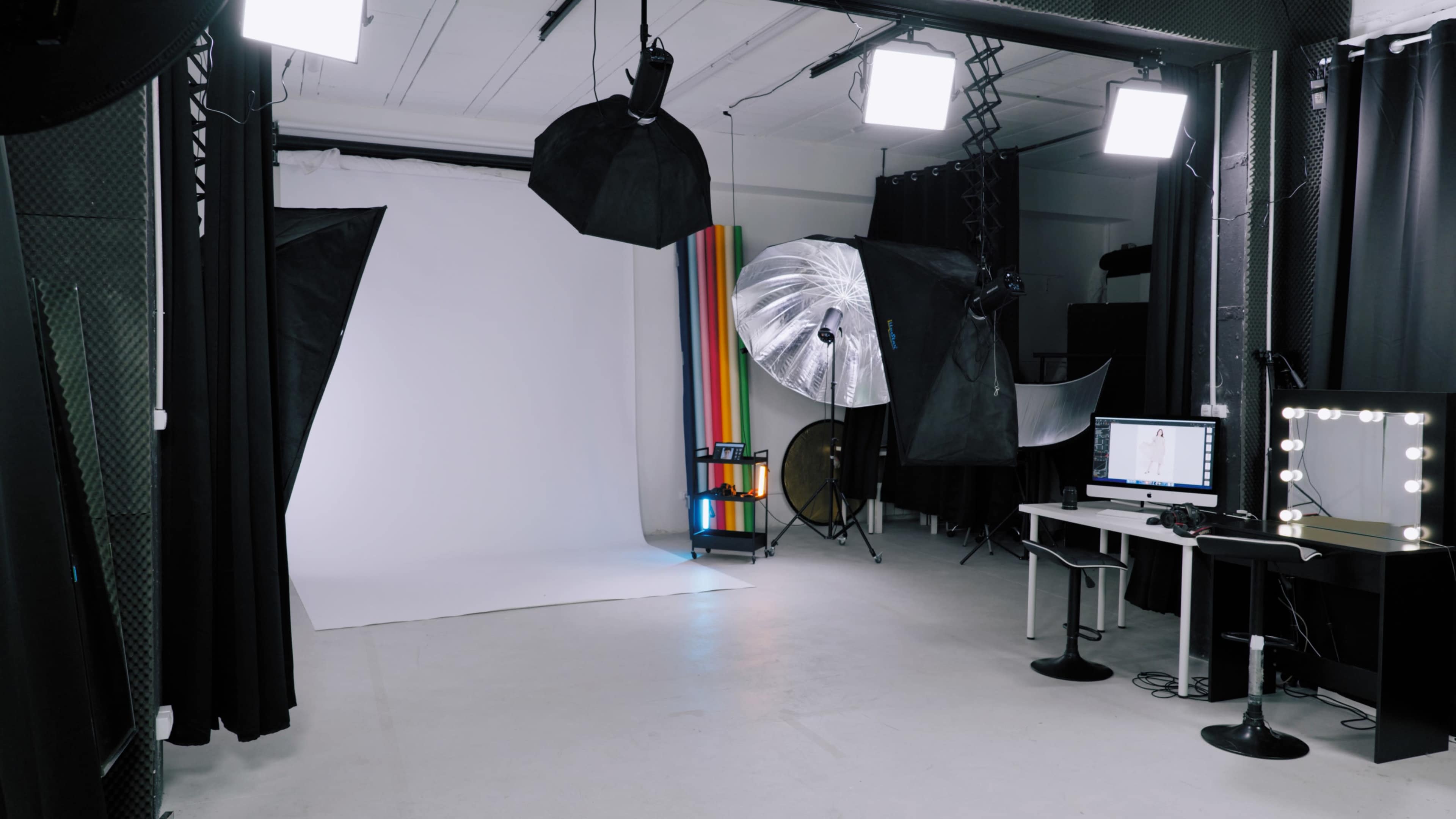 A photography studio with a white backdrop, lighting equipment, and a computer setup.