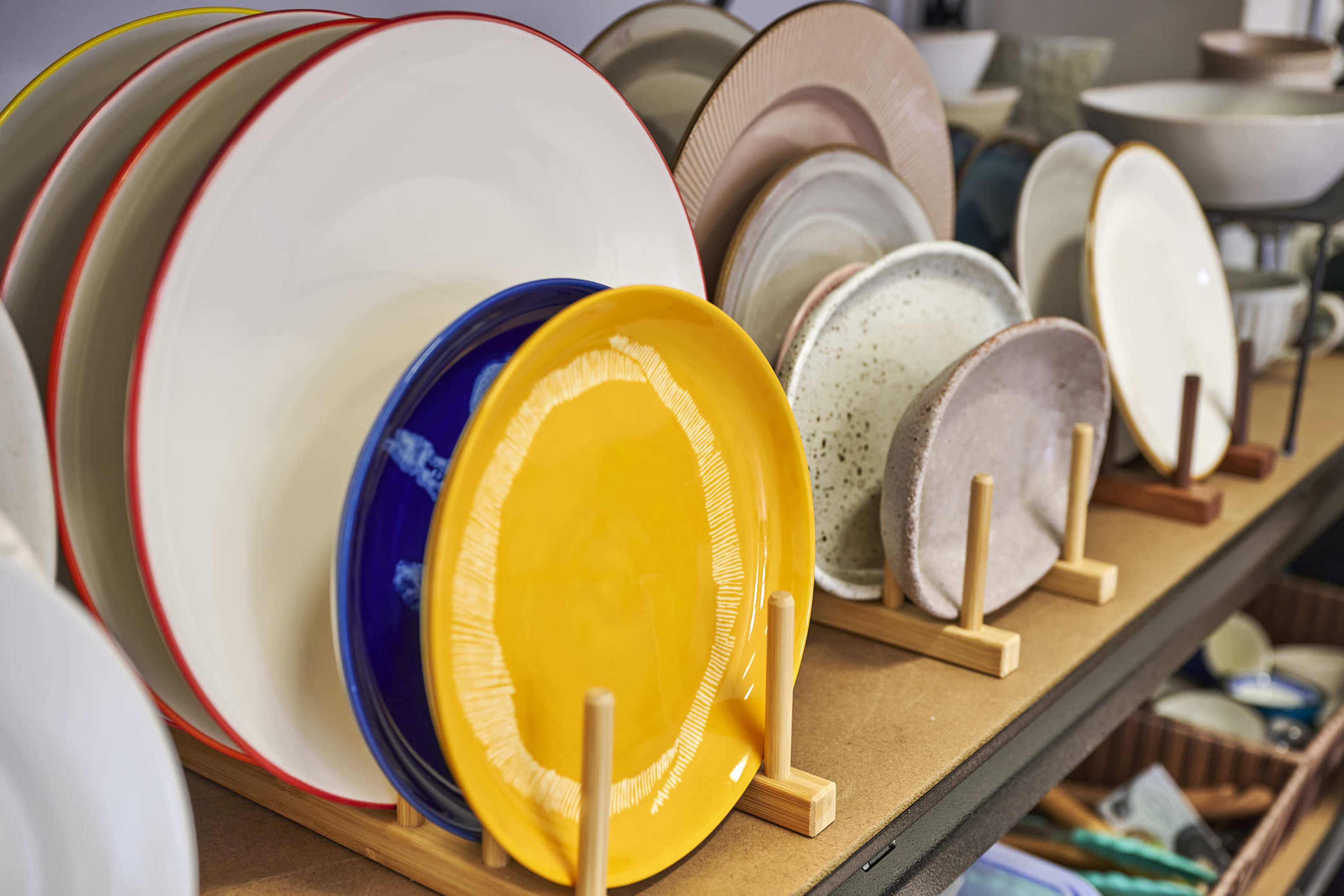 A collection of plates displayed on wooden stands, with varying colors and designs arranged neatly on a shelf.