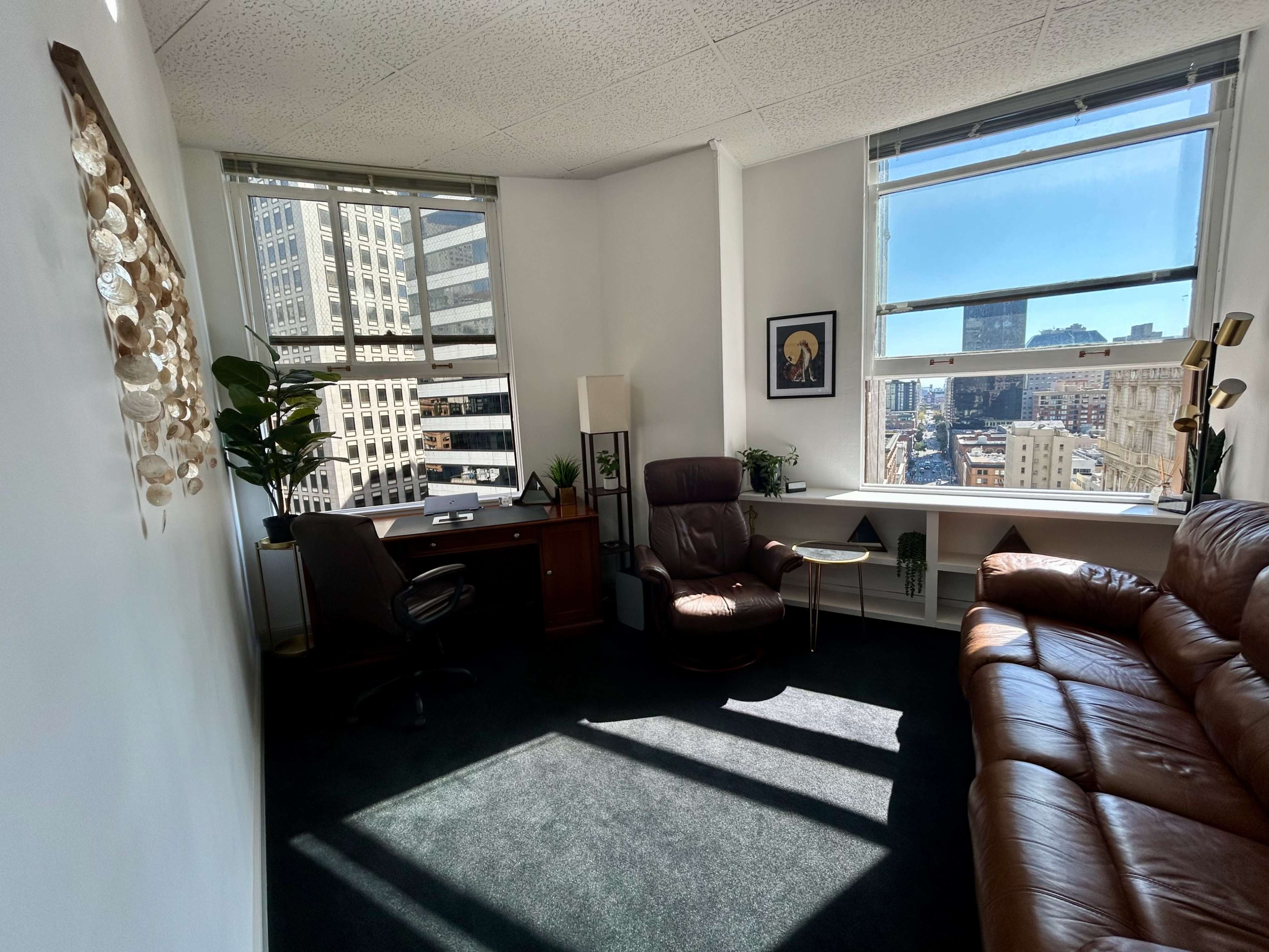 A bright office space with a desk, a leather recliner, and a window offering a view of a city skyline.