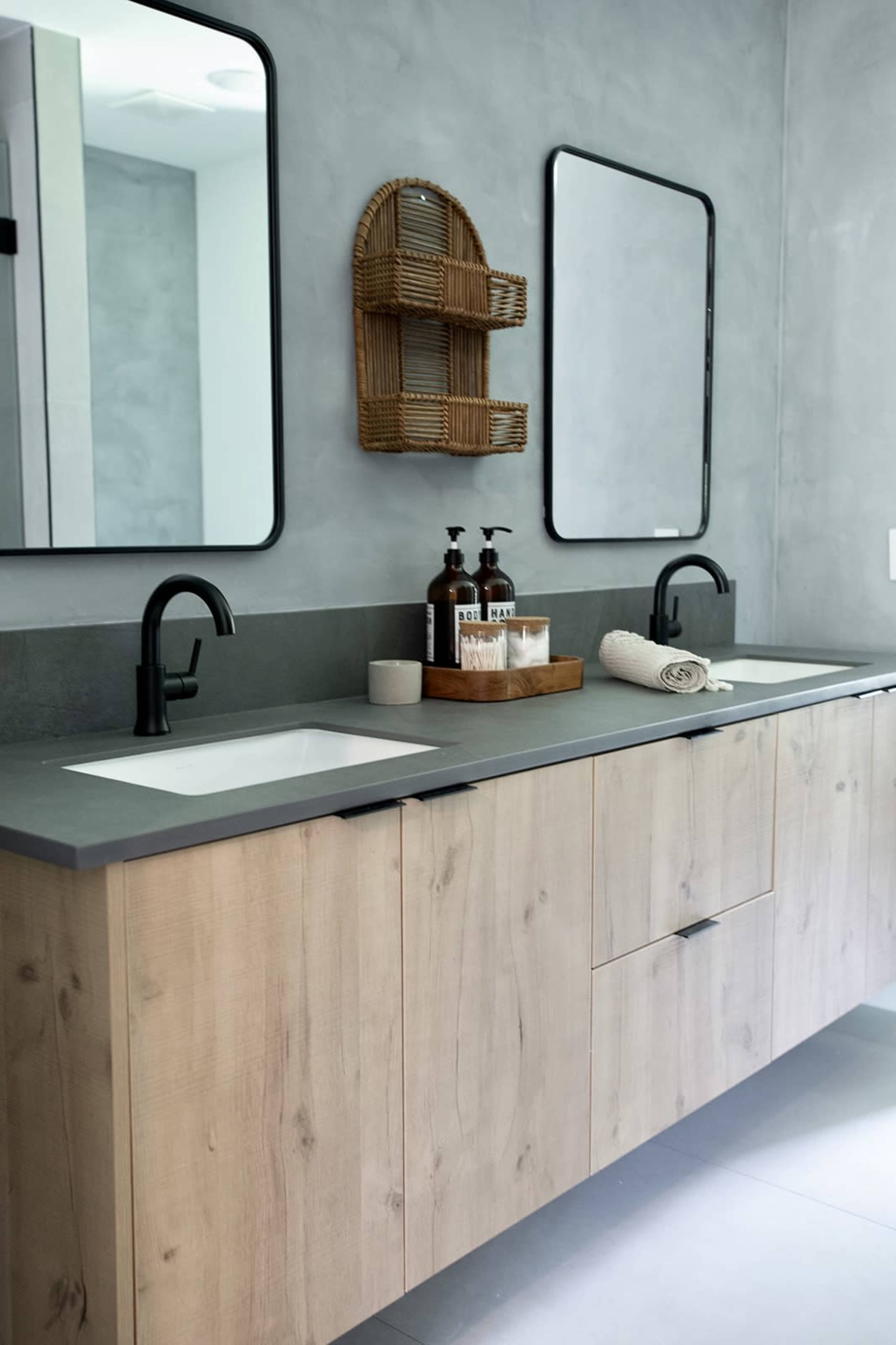 A modern bathroom with dual sinks, a wooden vanity, and two framed mirrors against a gray wall.