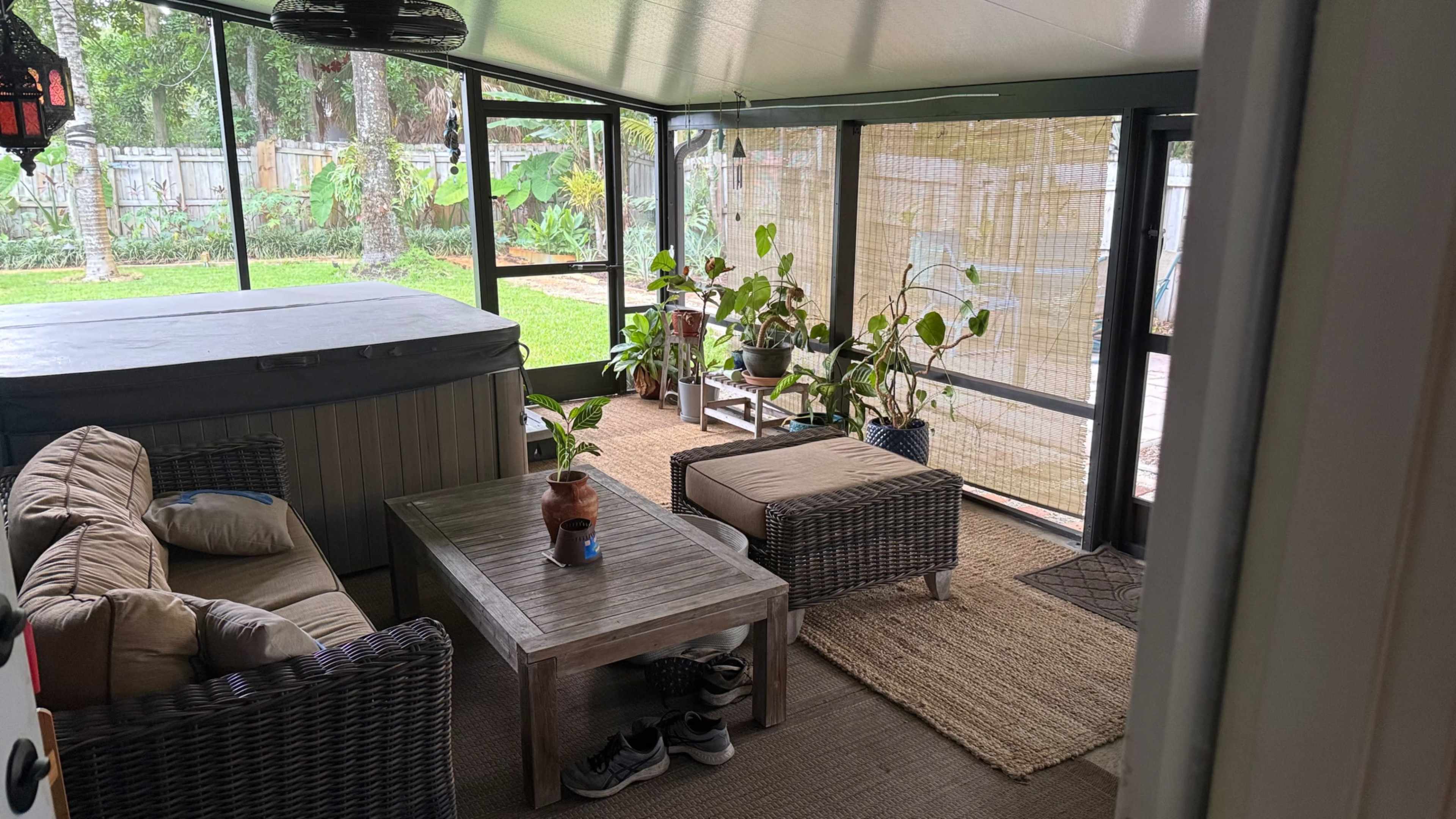 The image shows a screened-in patio area with a hot tub, seating arrangement, and several potted plants.