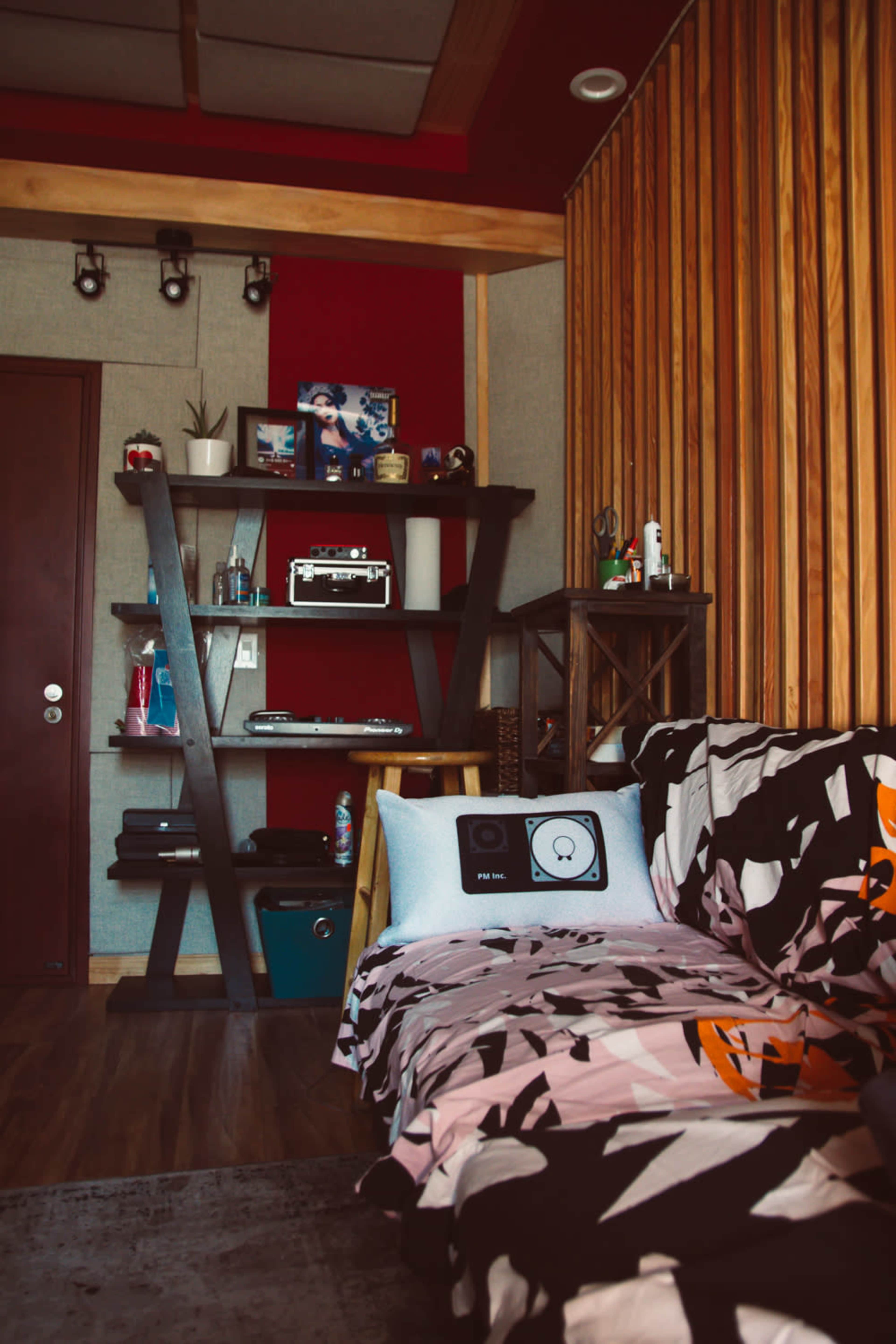 The image shows a cozy room featuring a wooden shelf with various items, a door, and a couch covered with a patterned blanket.