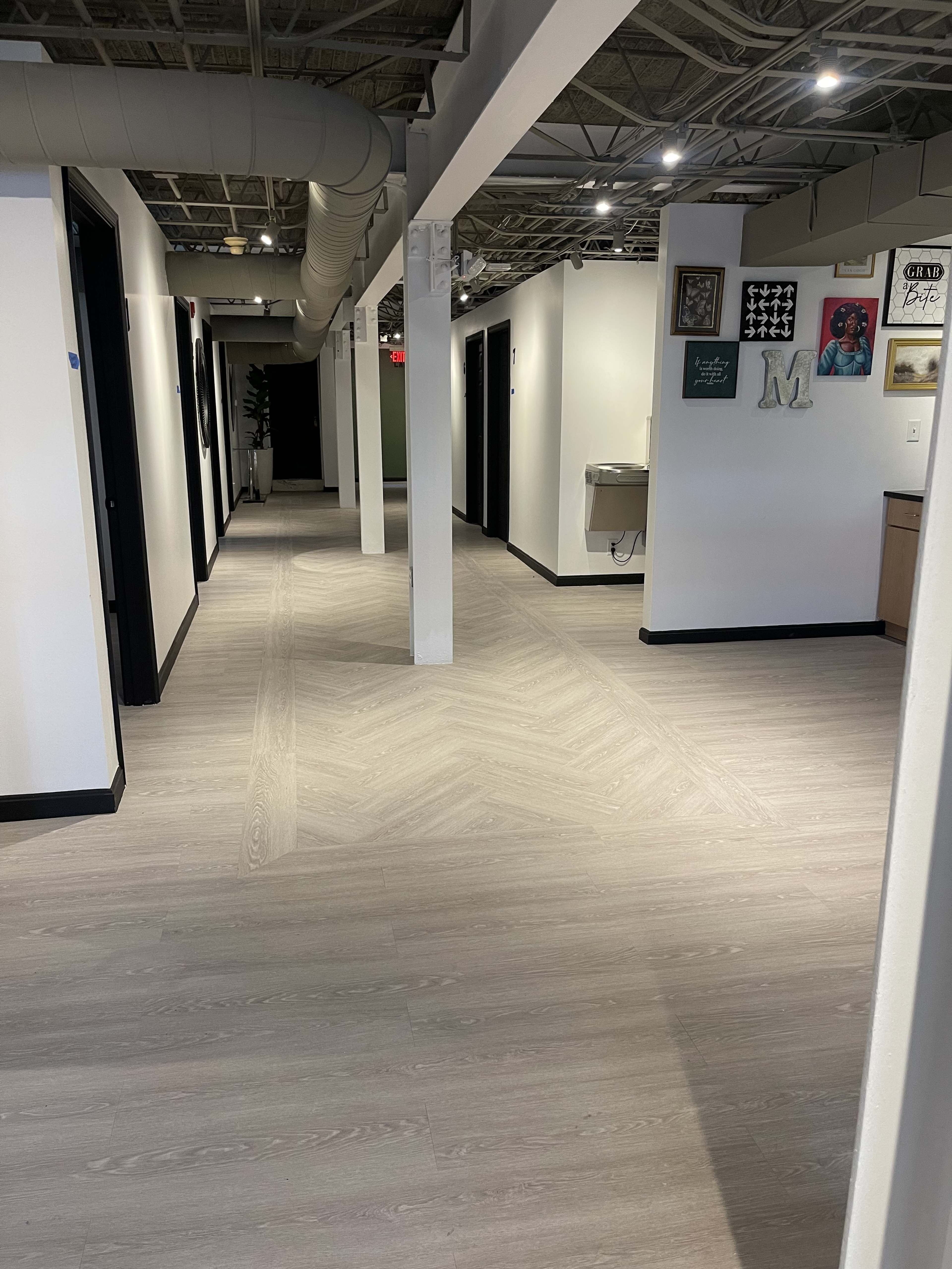 The image shows a modern office hallway with doors on both sides and light-colored flooring.