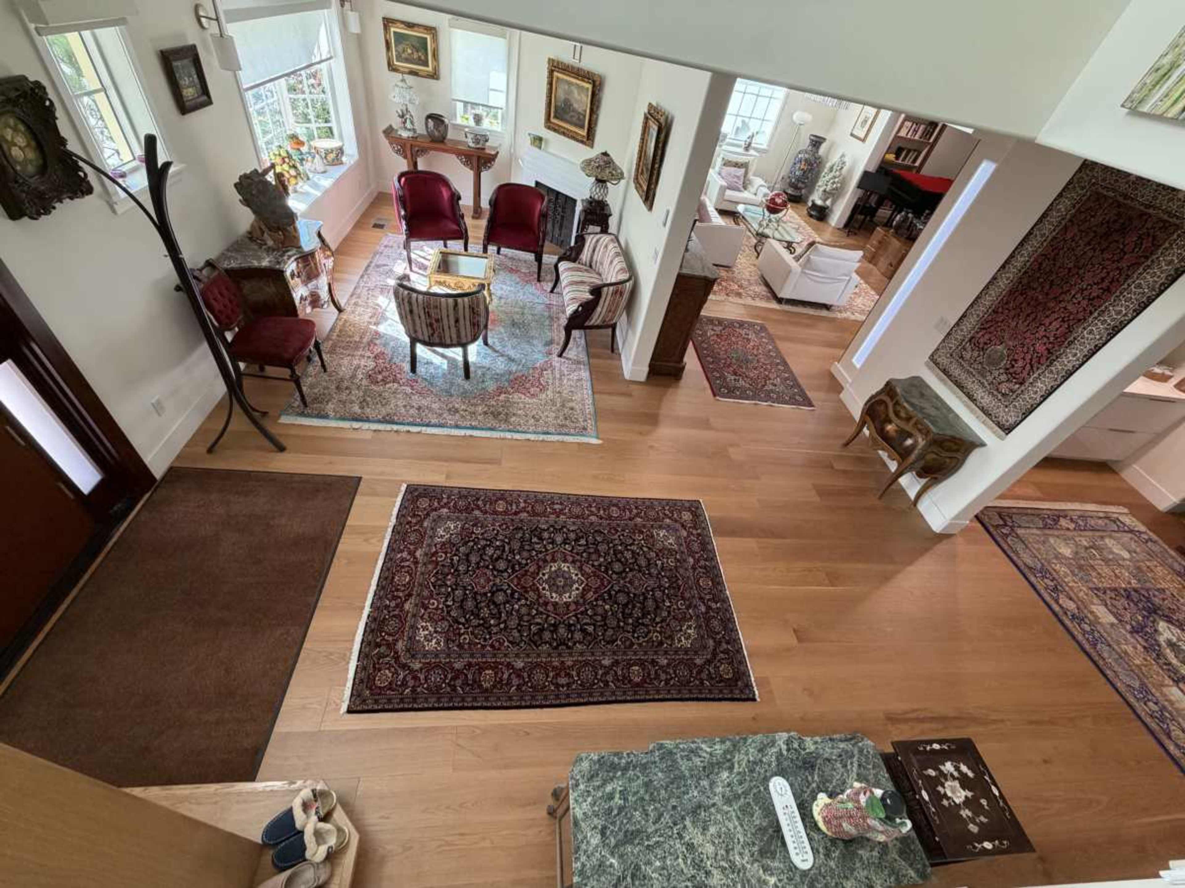 The image shows a spacious living area with a mix of seating arrangements, decorative rugs, and various artworks on the walls.