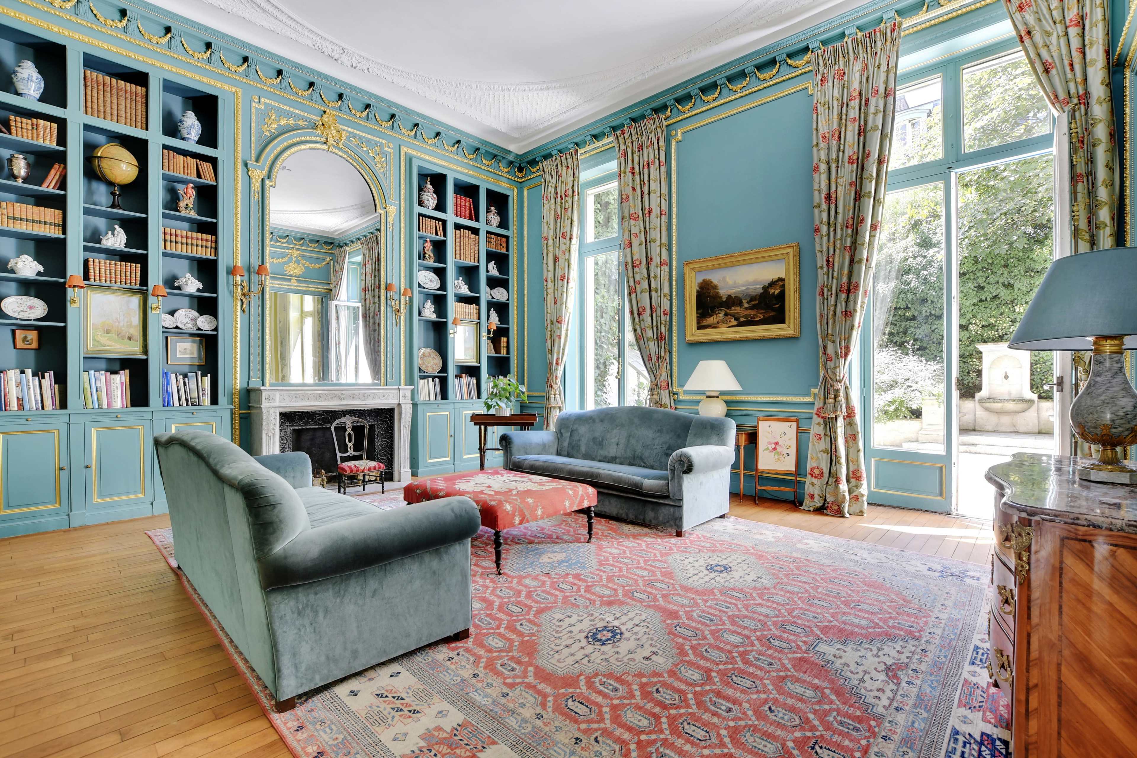 A beautifully furnished living room with light blue walls, large windows, and a central Persian rug.