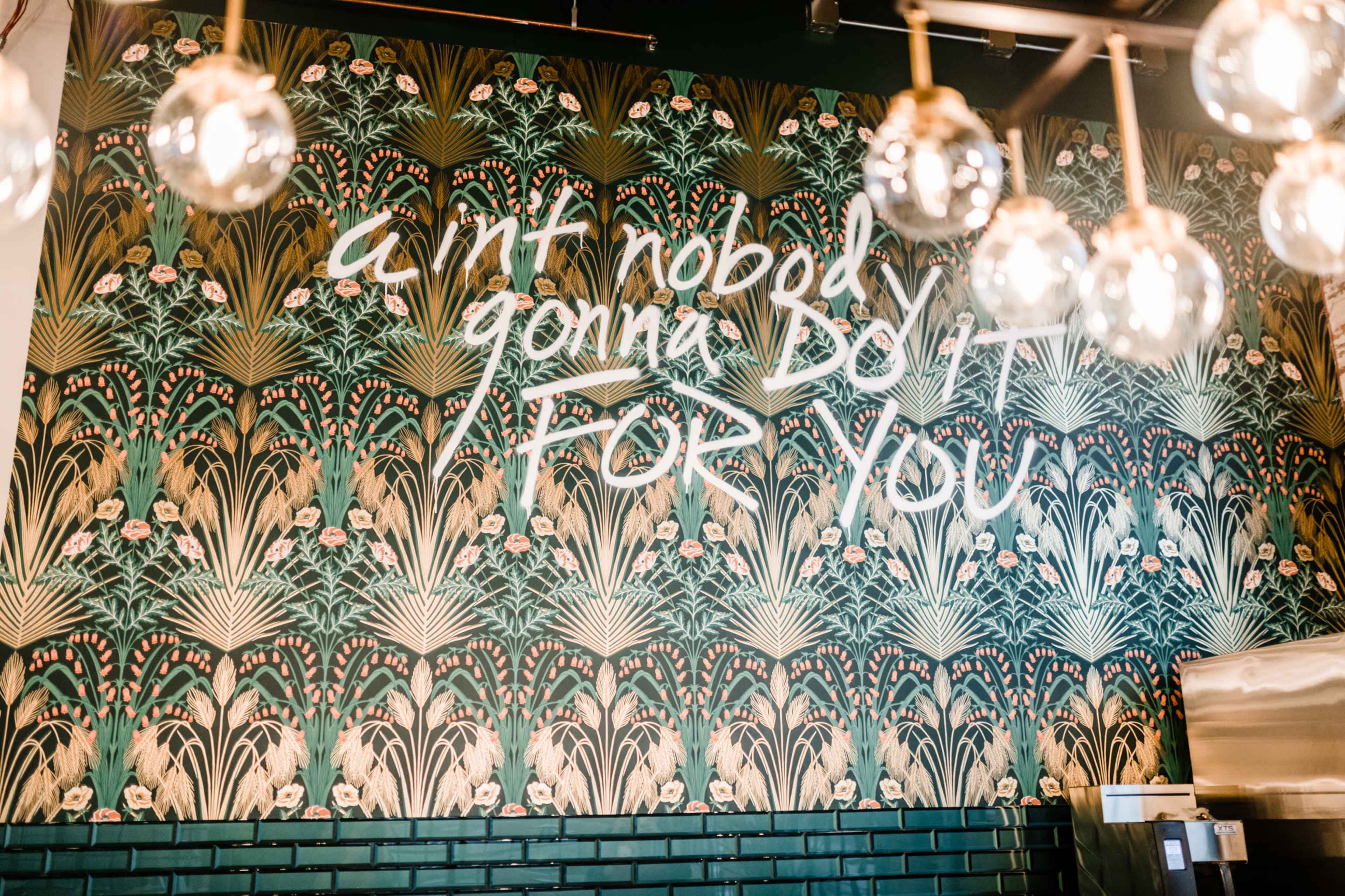 A colorful mural featuring the phrase "Ain't nobody gonna do it for you" against a decorative background of plants and flowers.