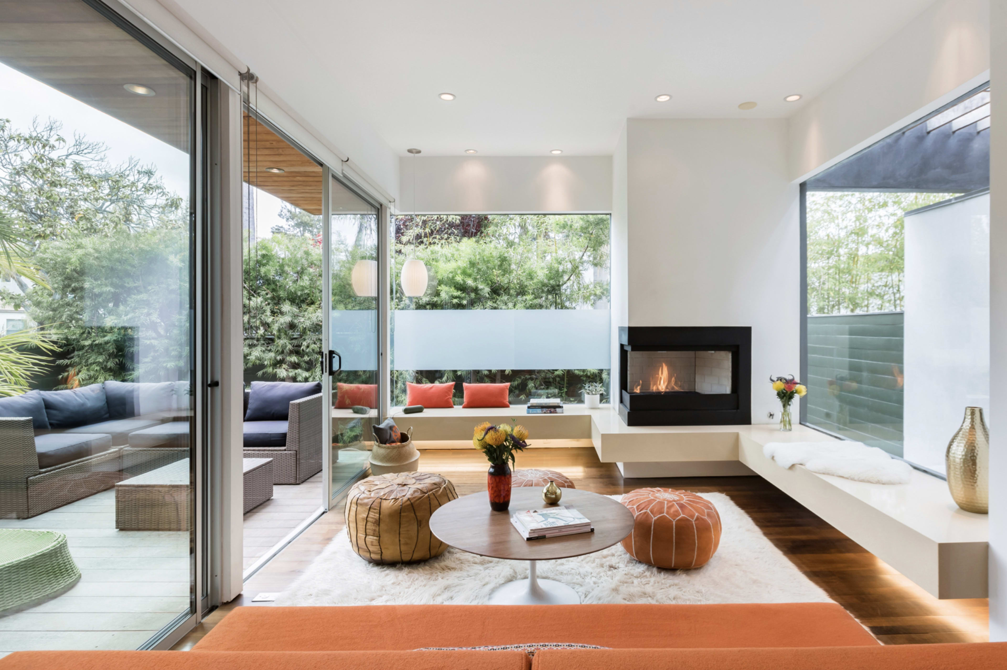 The image shows a modern living room with an open layout, featuring a fireplace, a circular coffee table, and large windows that provide natural light.