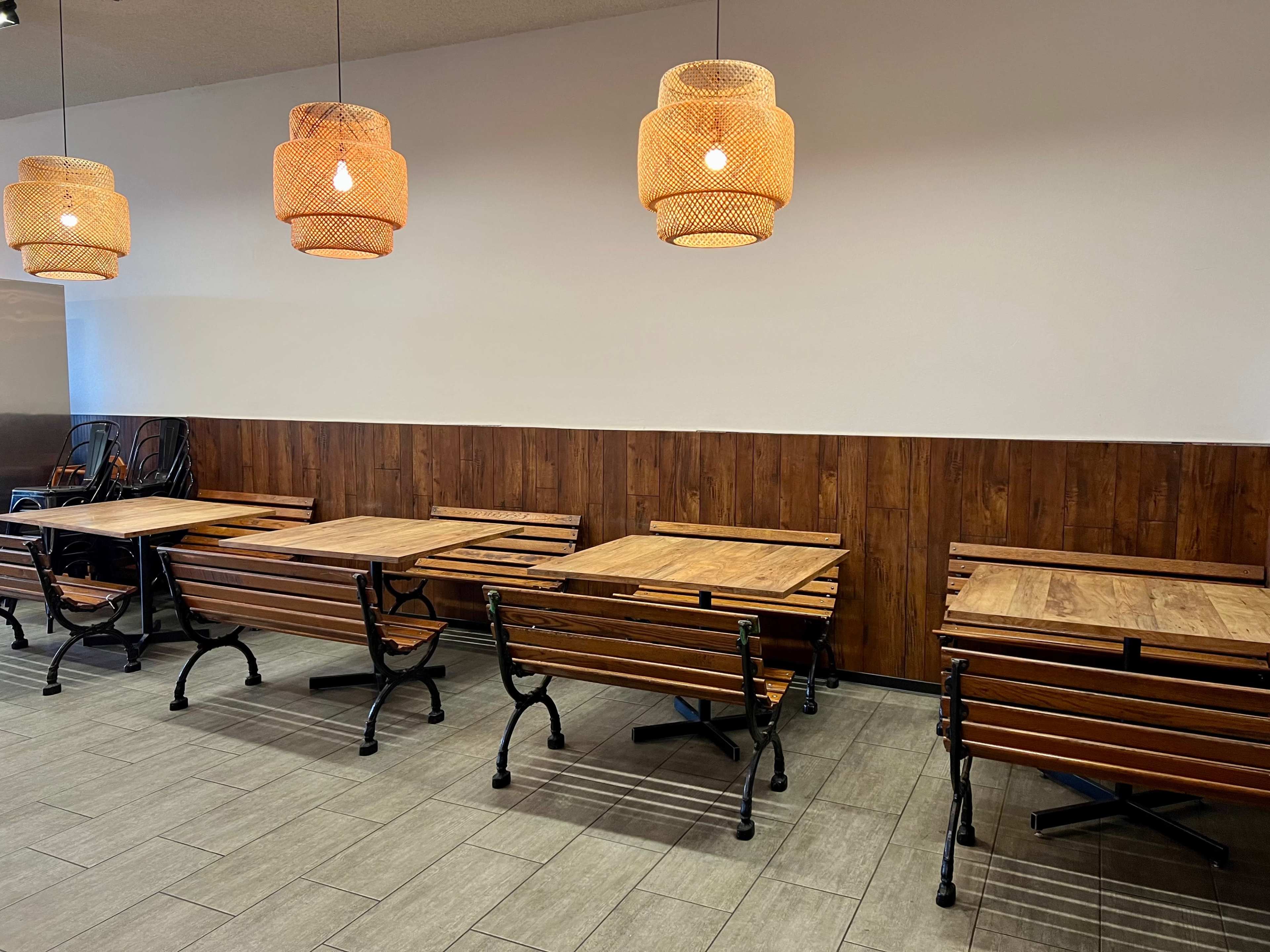 The image shows a dining area with wooden tables and benches arranged under pendant lights.