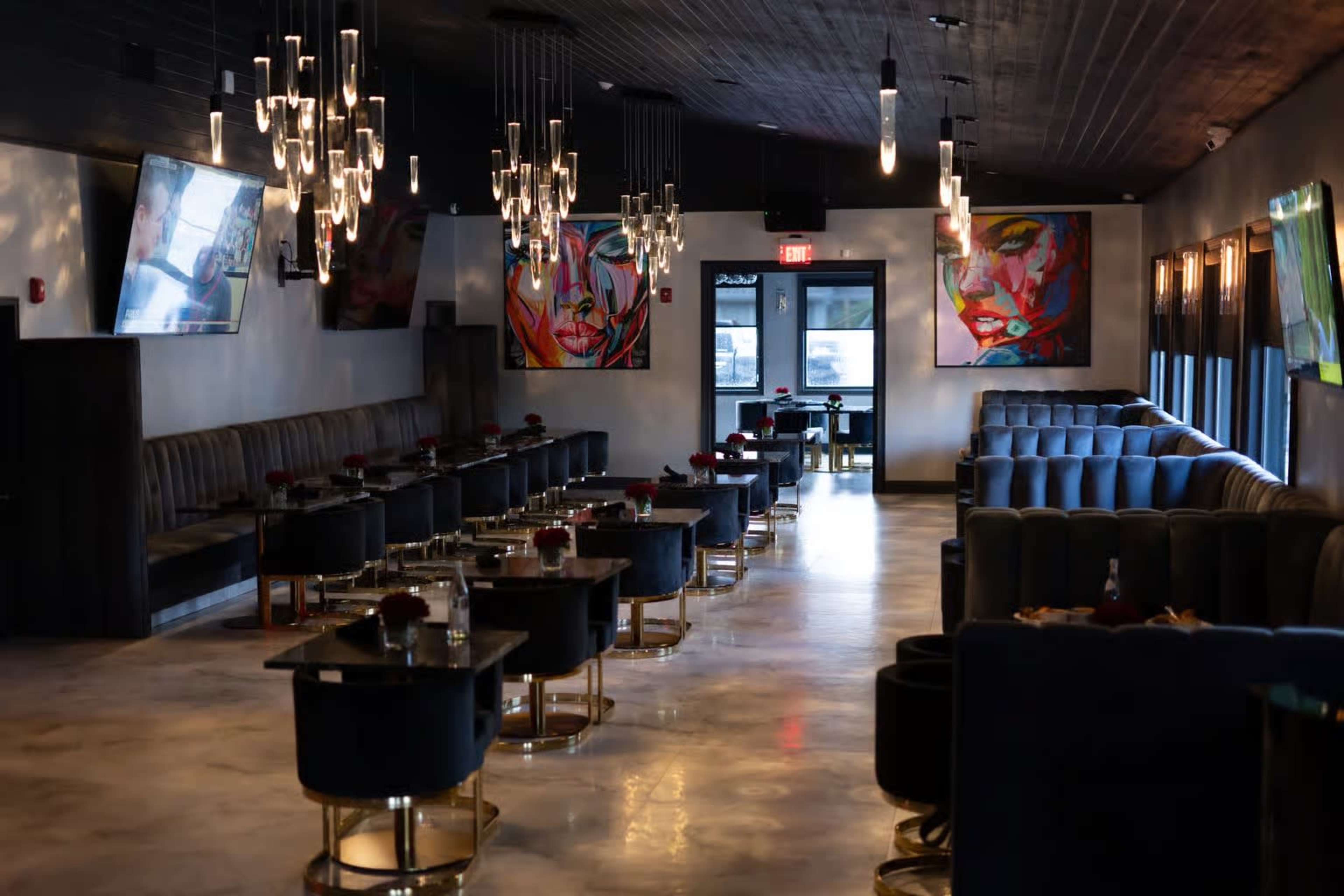The image shows a modern restaurant interior featuring dark seating, sleek tables, abstract artwork on the walls, and pendant lighting.