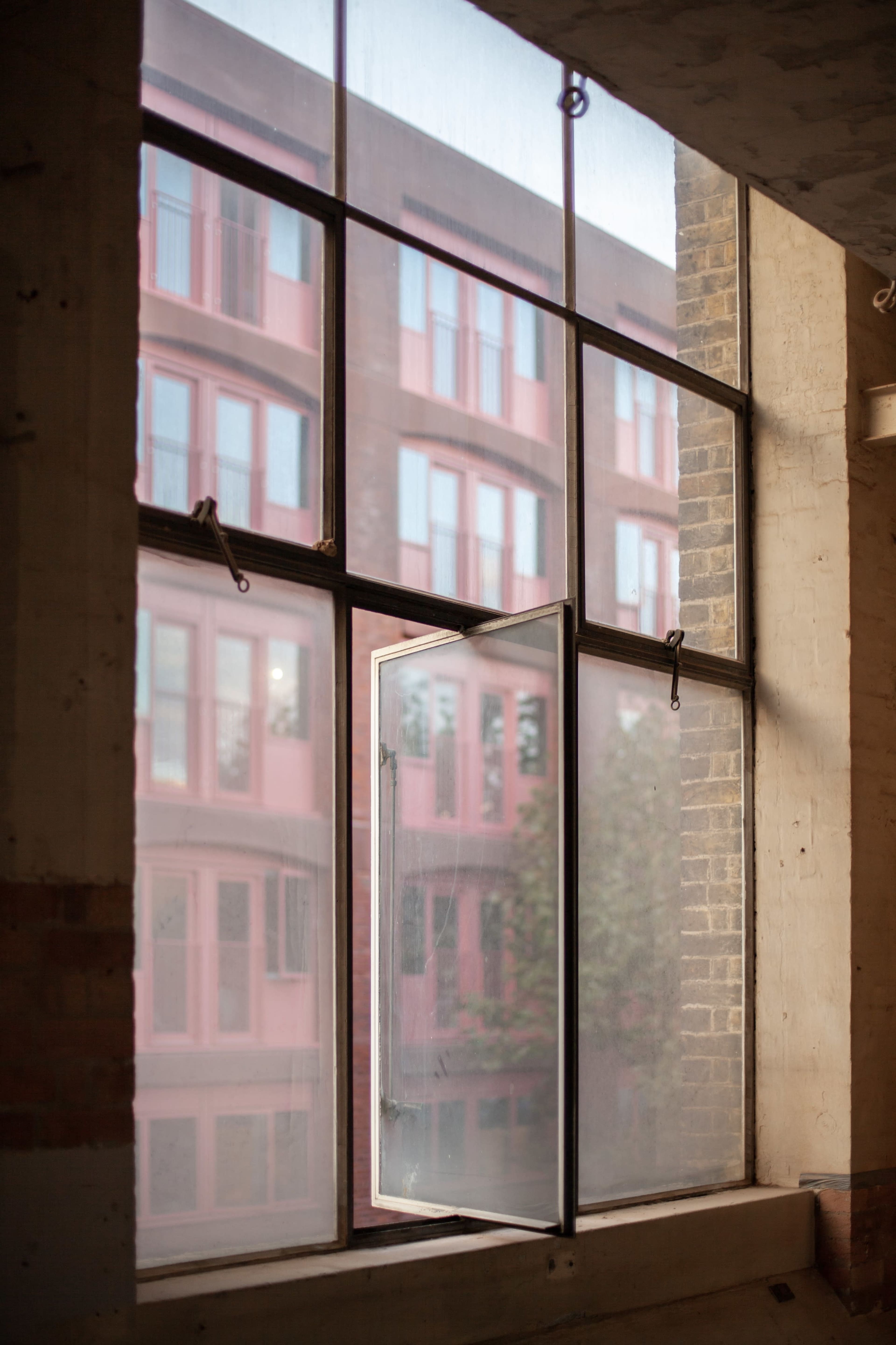 An open window reveals a view of pink-framed windows on a building across the street.