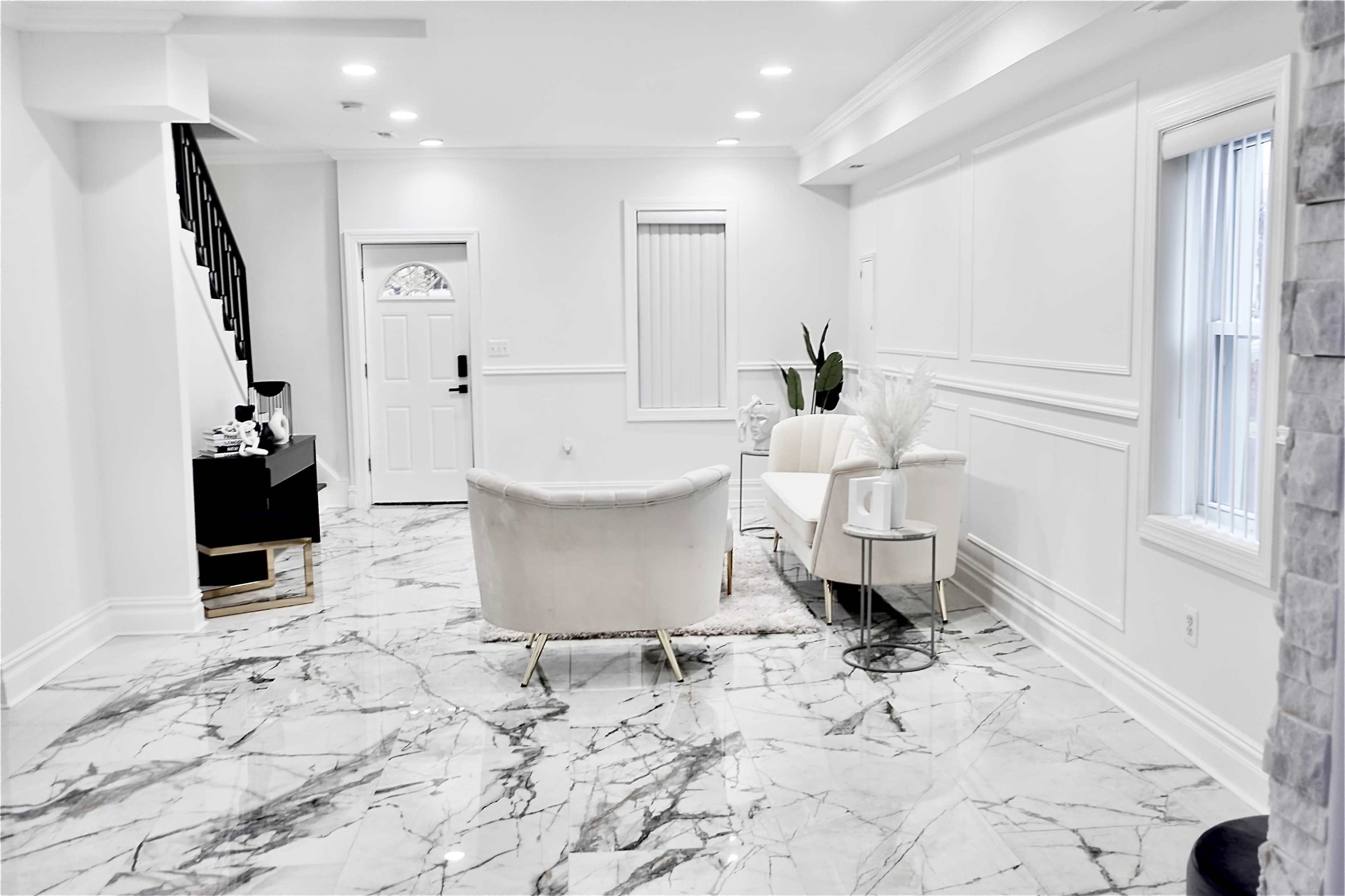 A modern living room with marble flooring, a white seating area, and a staircase leading to another level.