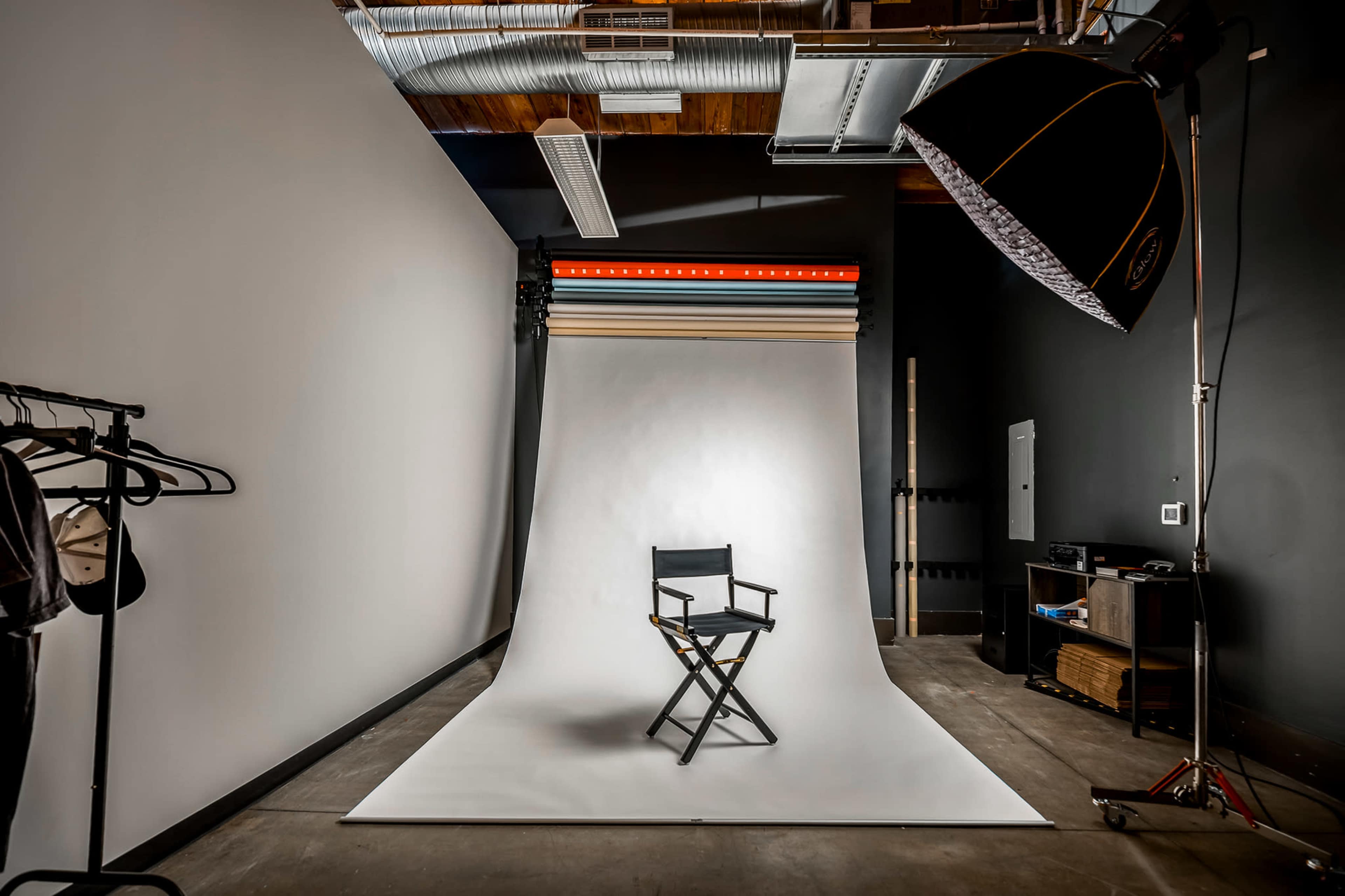 A photography studio features a white backdrop, a director's chair, and various equipment for photo shoots.