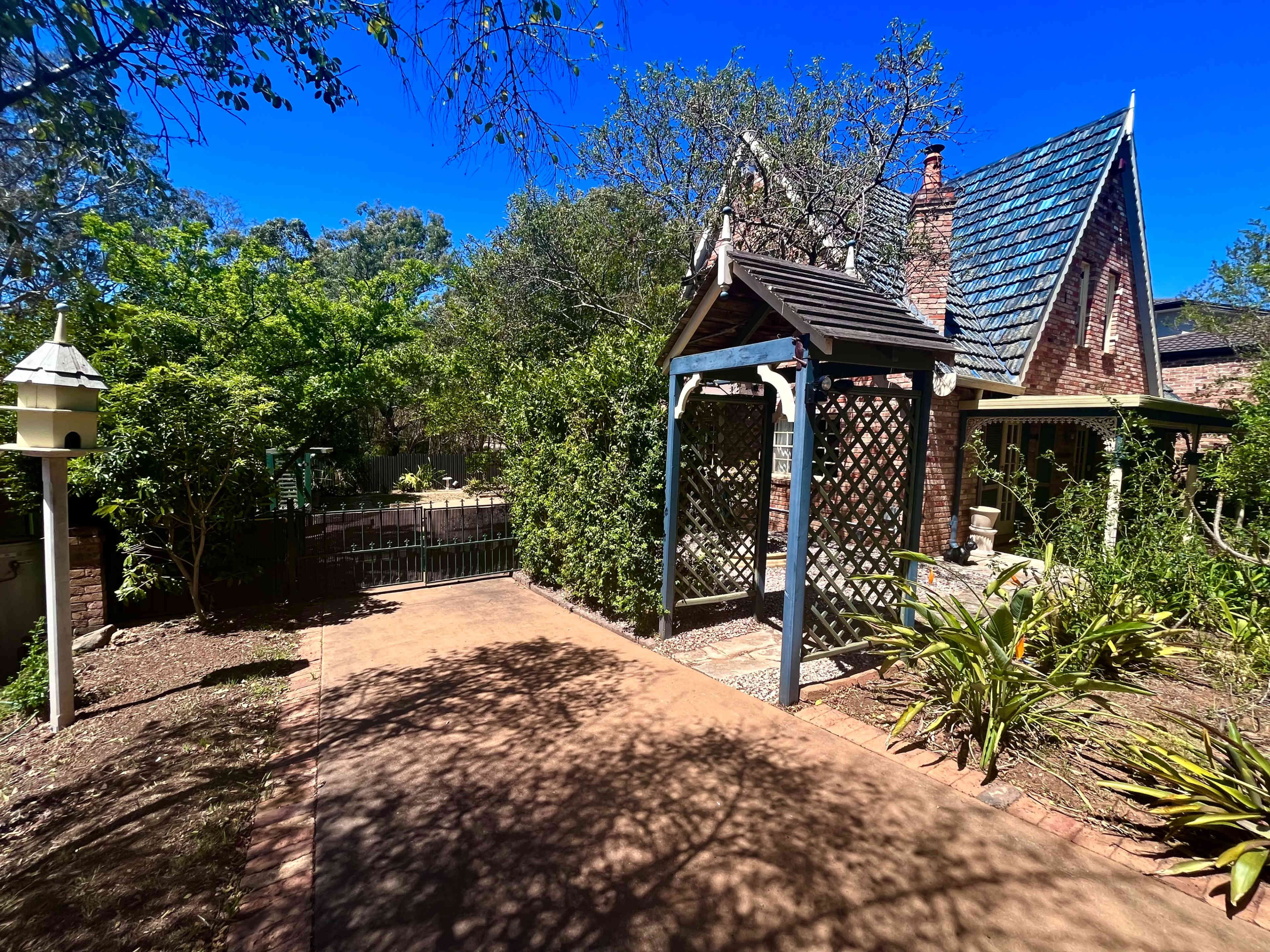 A pathway leading to a house with a peaked roof, surrounded by greenery and a trellis structure.