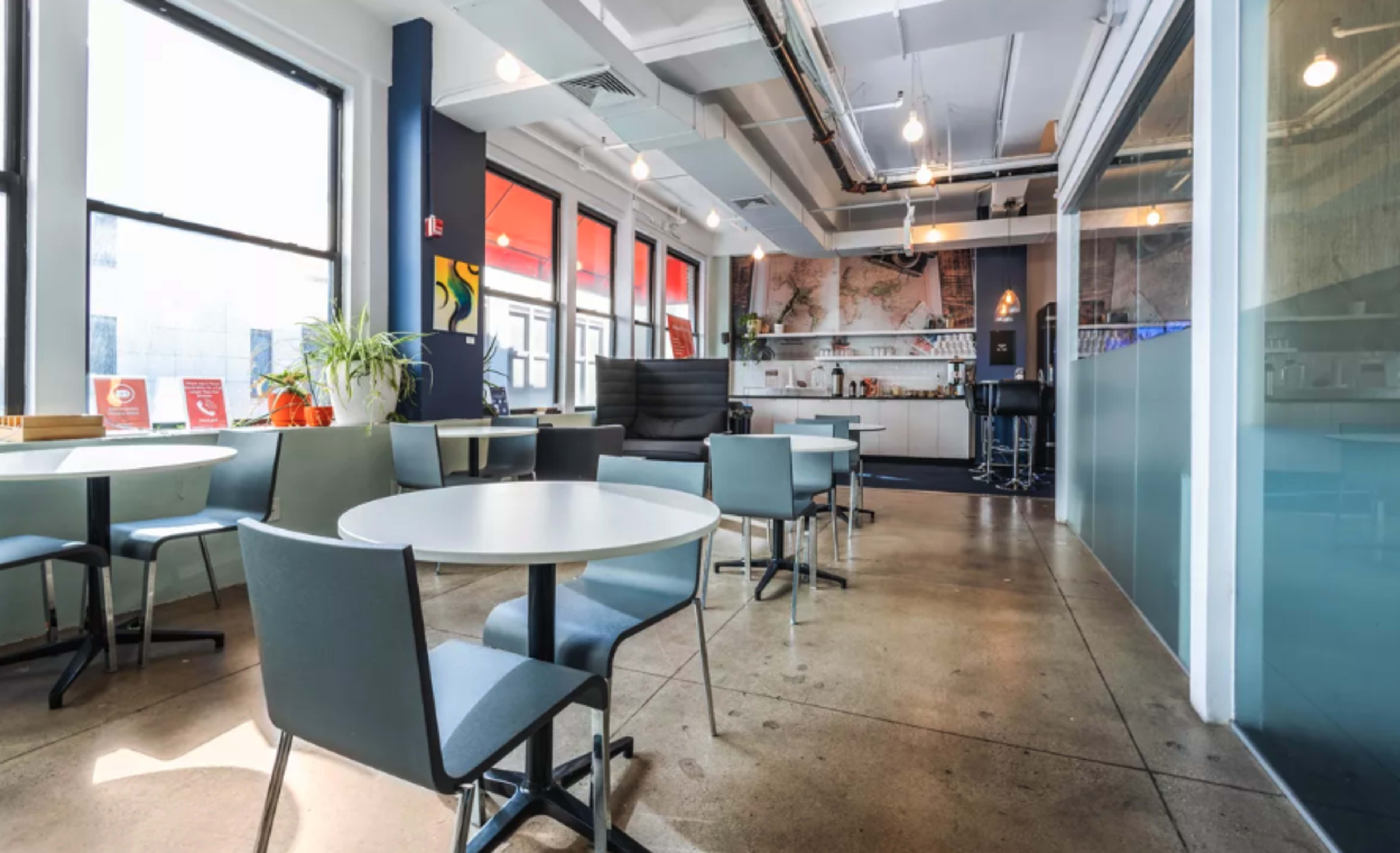 A modern café interior with several tables and chairs, large windows, a bar area, and colorful wall decor.