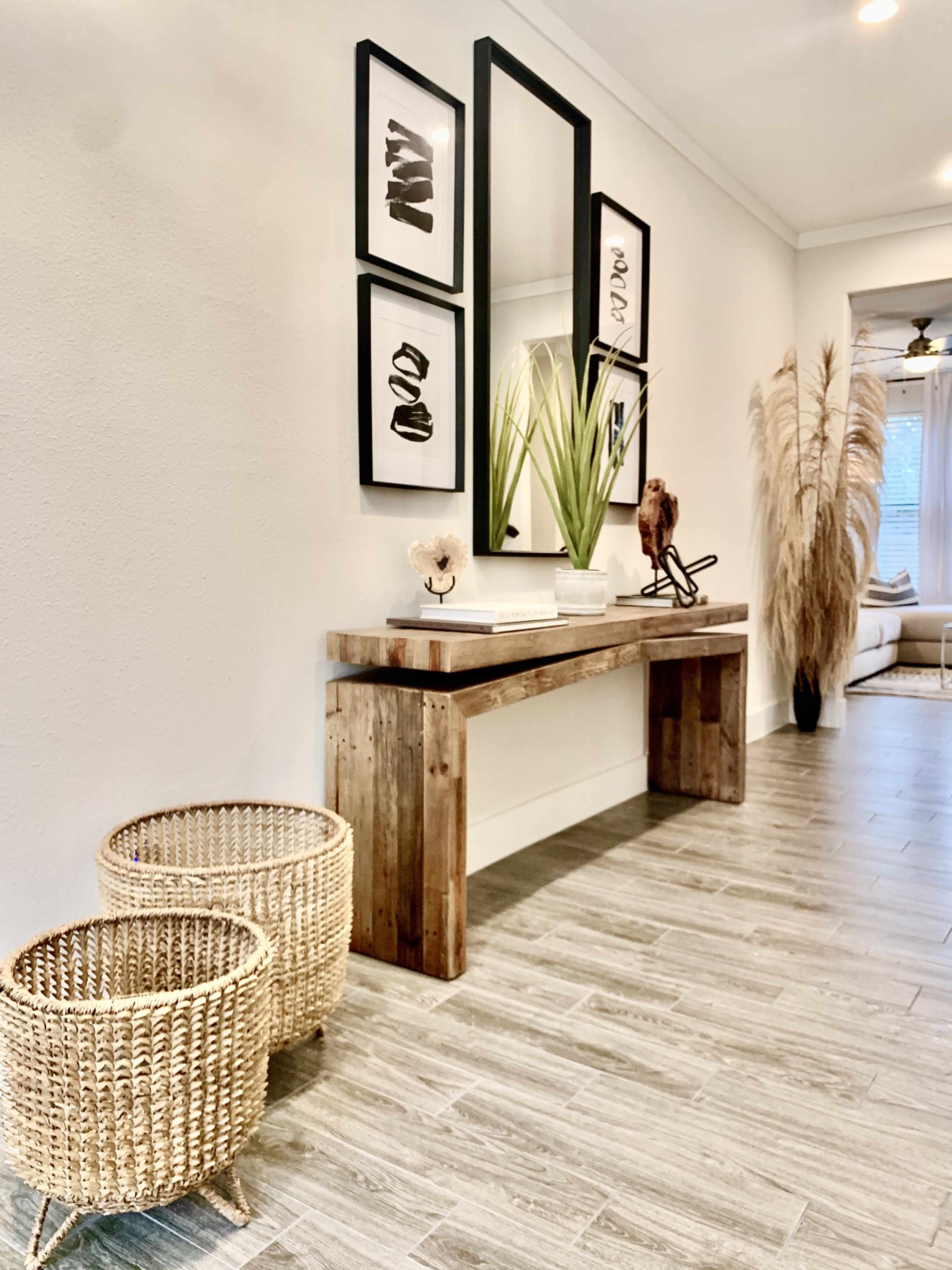 A hallway with a wooden console table adorned with decorative items, flanked by two woven baskets and framed black-and-white art on the wall.