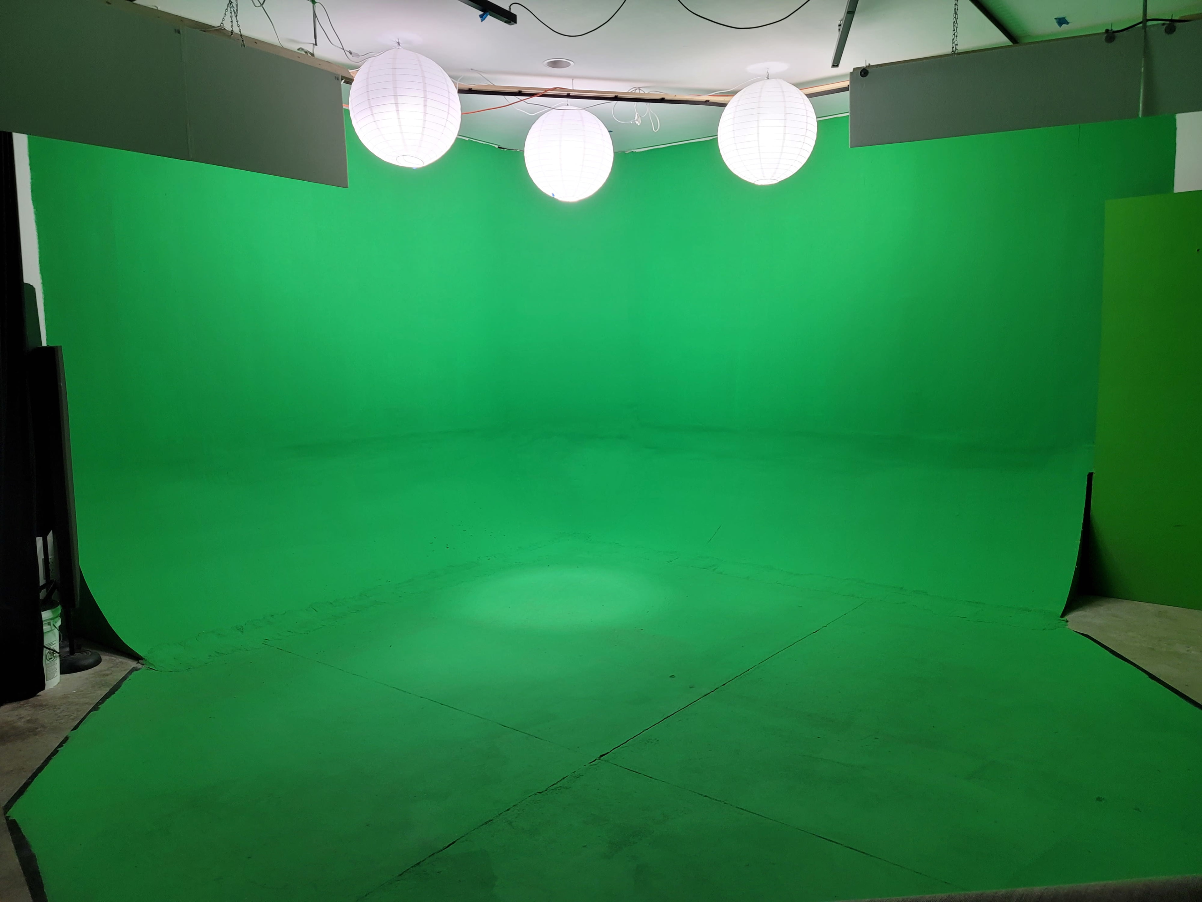 The image shows a spacious green screen studio with three overhead lanterns providing illumination.