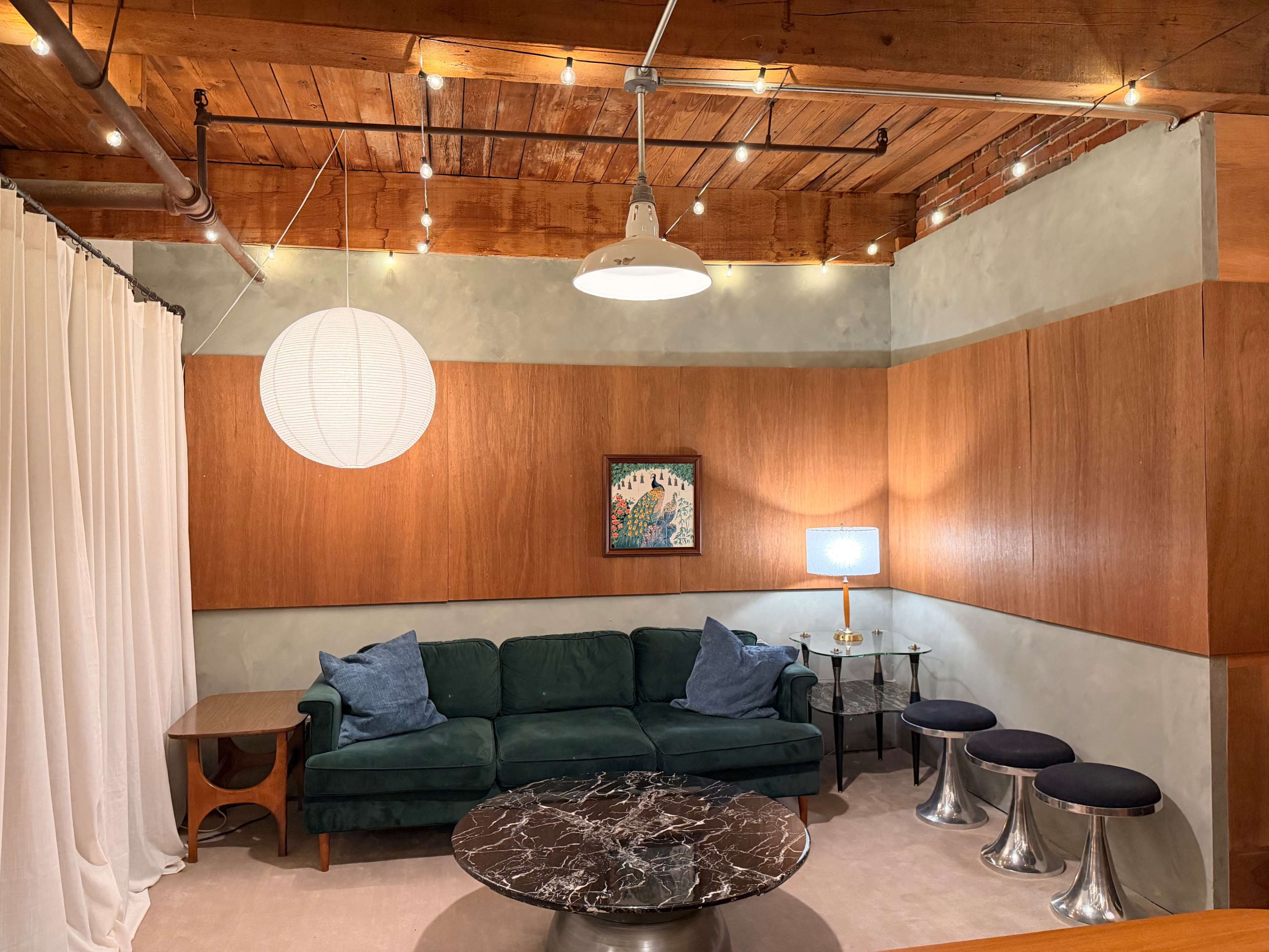 The image depicts a modern living room with a green couch, a marble coffee table, wooden paneling, and soft lighting from a pendant lamp.
