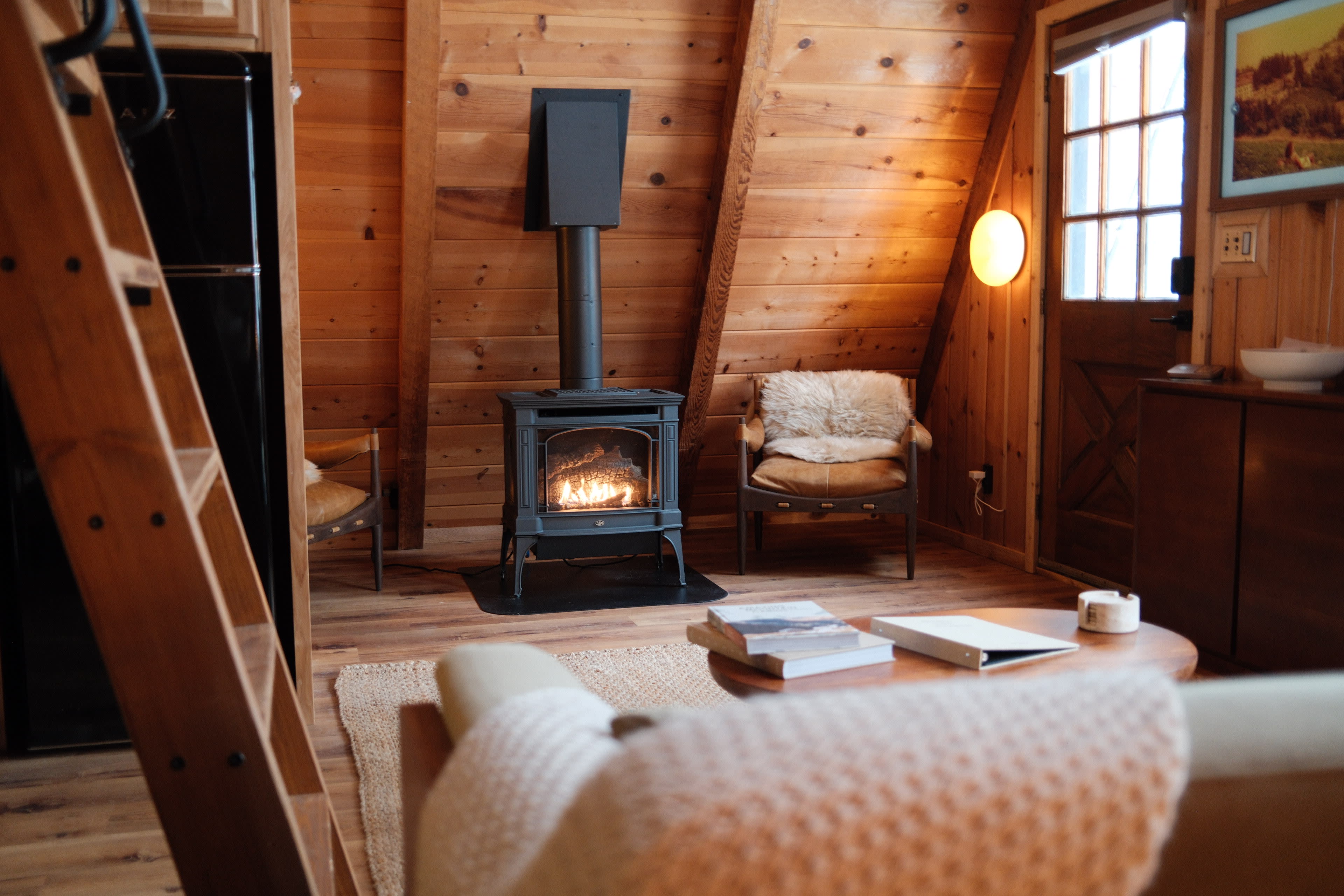 The image shows a cozy cabin interior with wooden walls, a wood-burning stove, and comfortable seating.