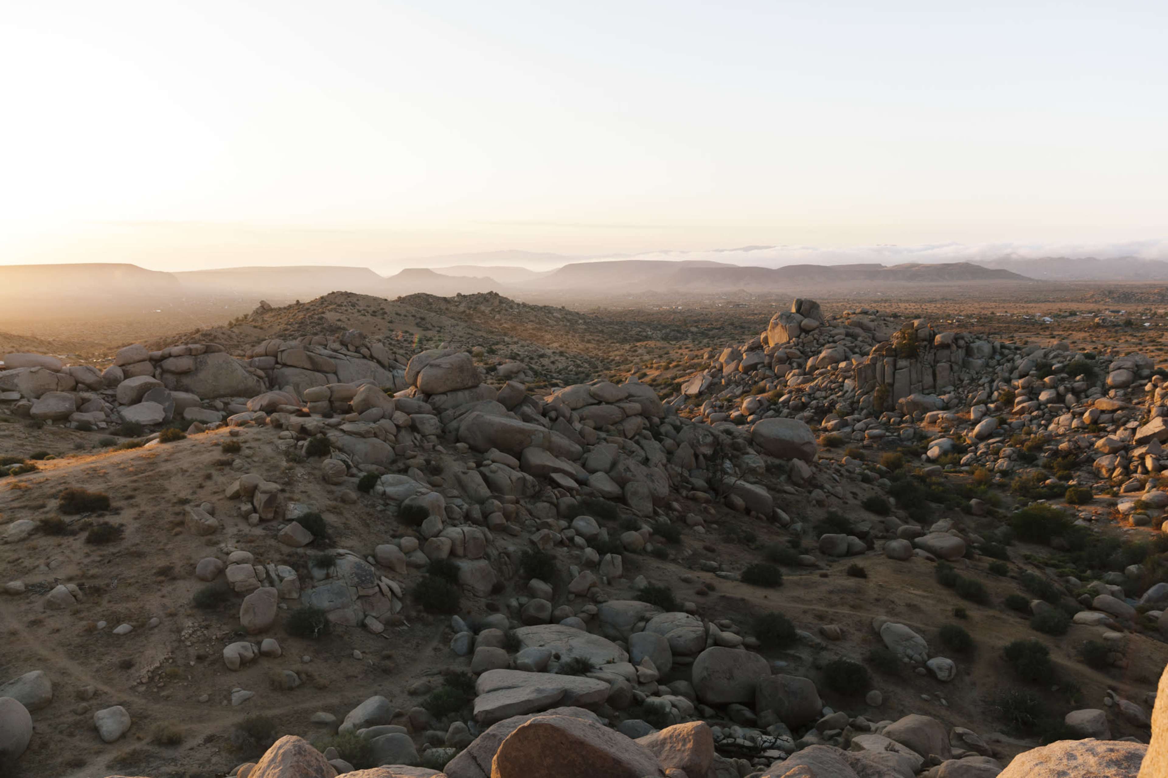A rocky landscape with large boulders and distant mountains under a soft sunset light.