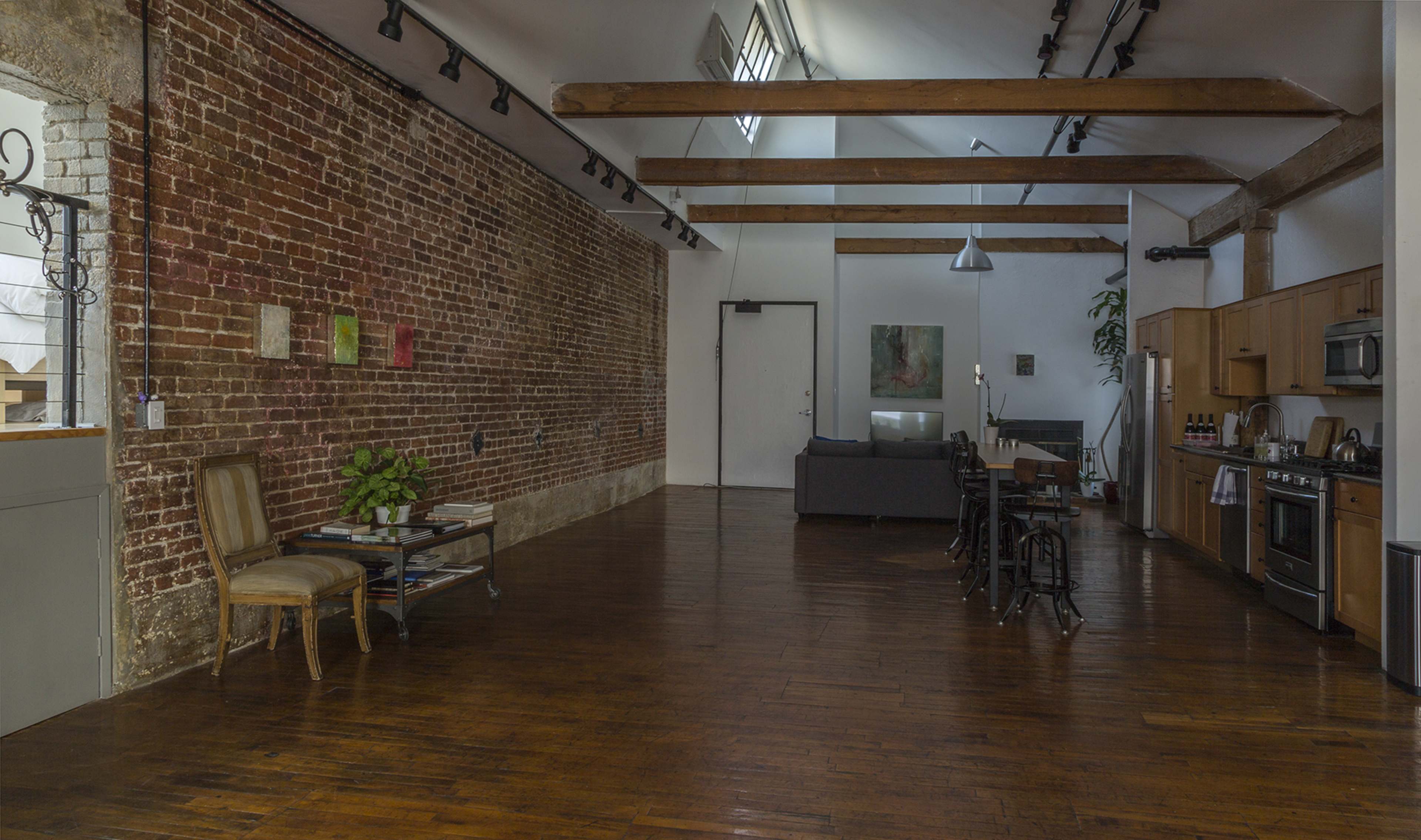 A spacious, open-concept loft with exposed brick walls, wooden beams, and a mix of modern and vintage furnishings.