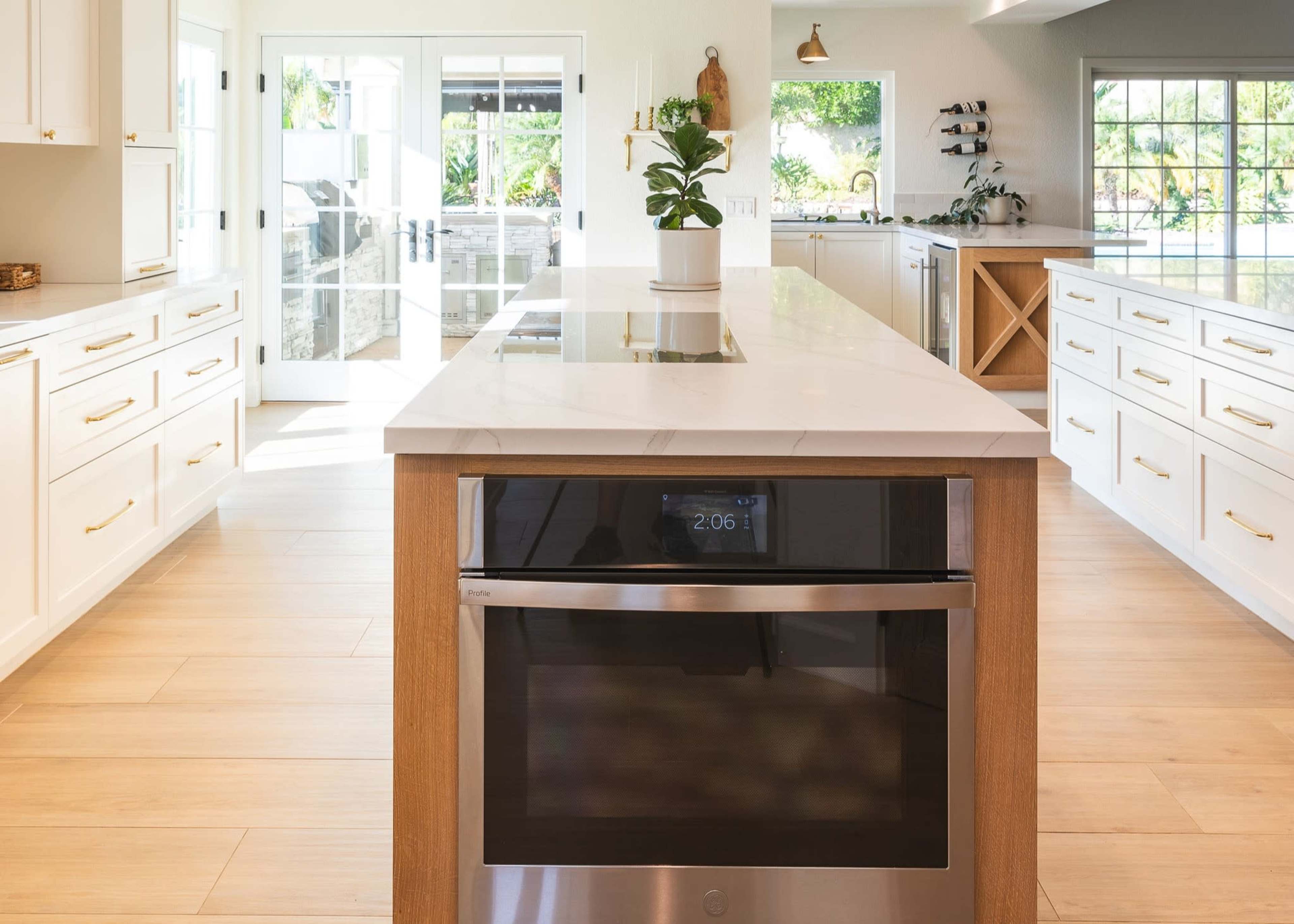 A modern kitchen with a large island, equipped with a cooktop, stainless steel oven below, and bright natural light coming through the windows.