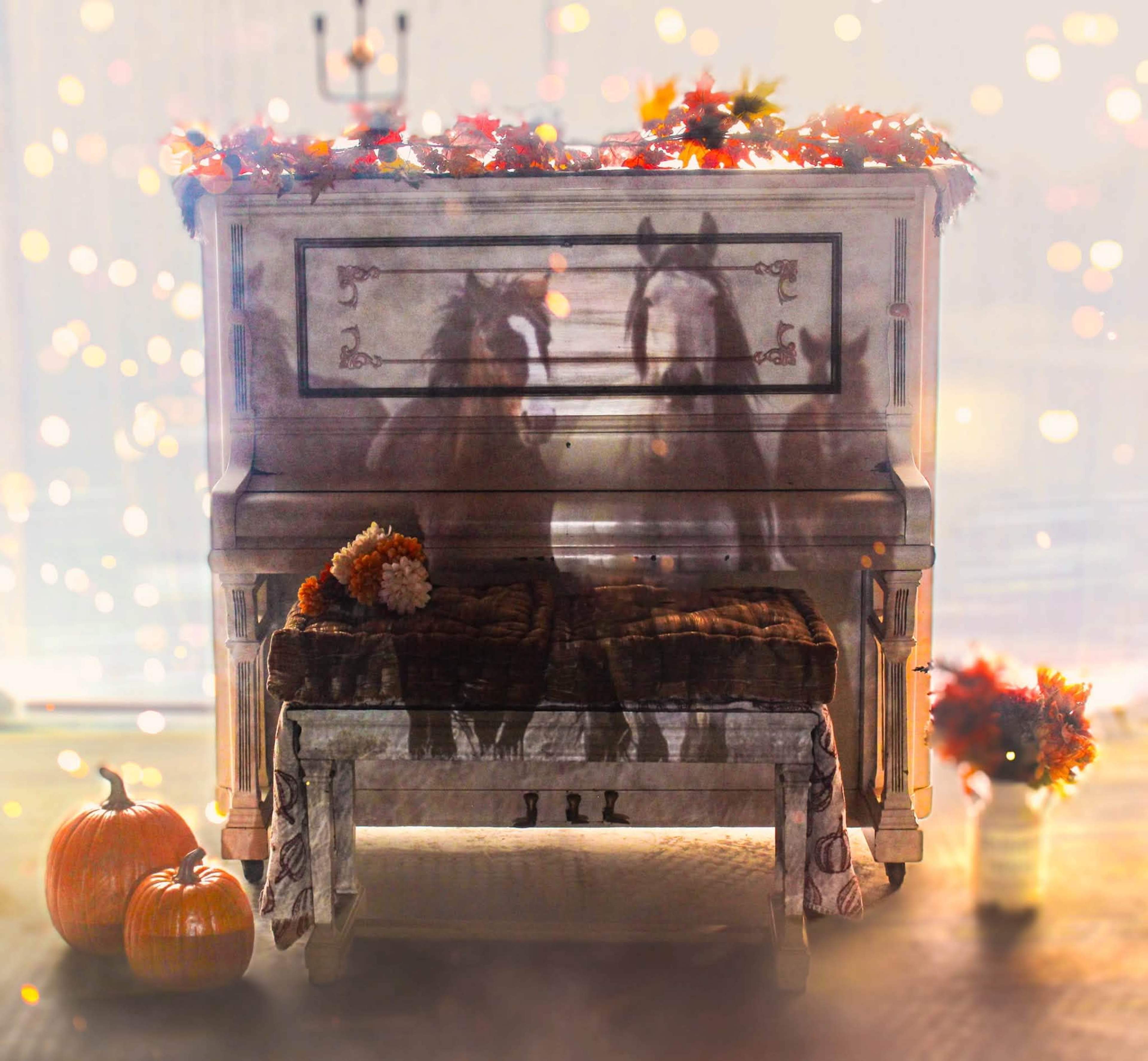 A vintage white piano with autumn decorations sits in a softly lit room alongside pumpkins and a bench.