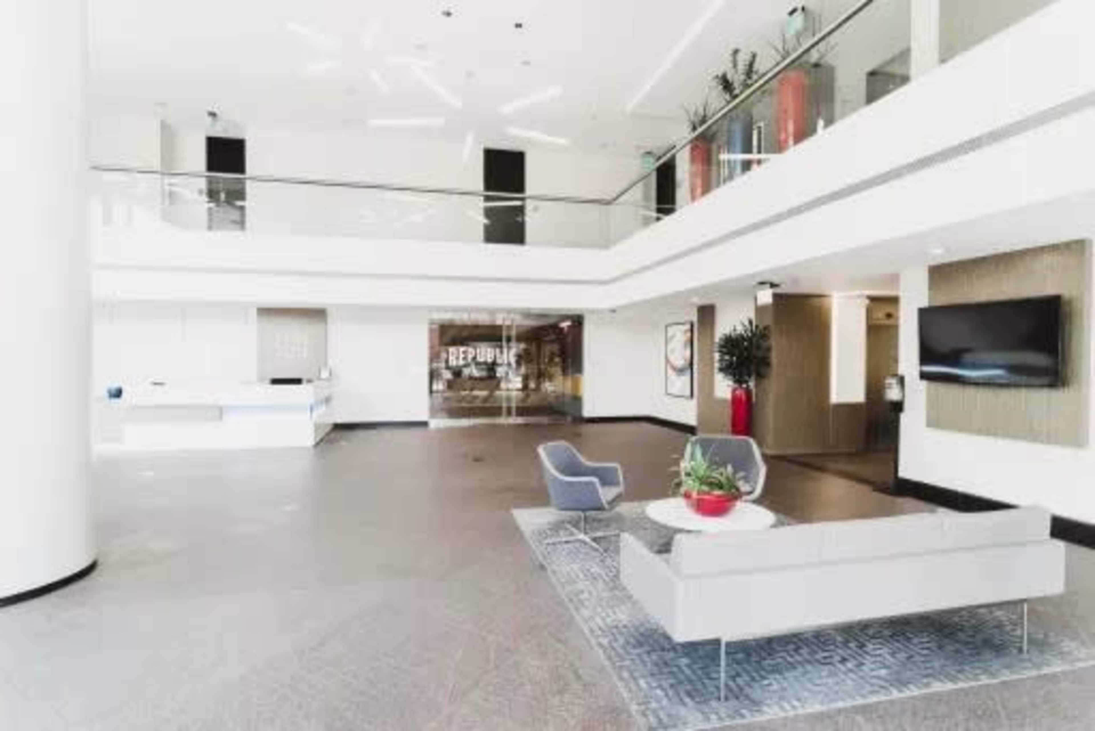 The image shows a modern lobby with a reception area, seating, and glass accents.
