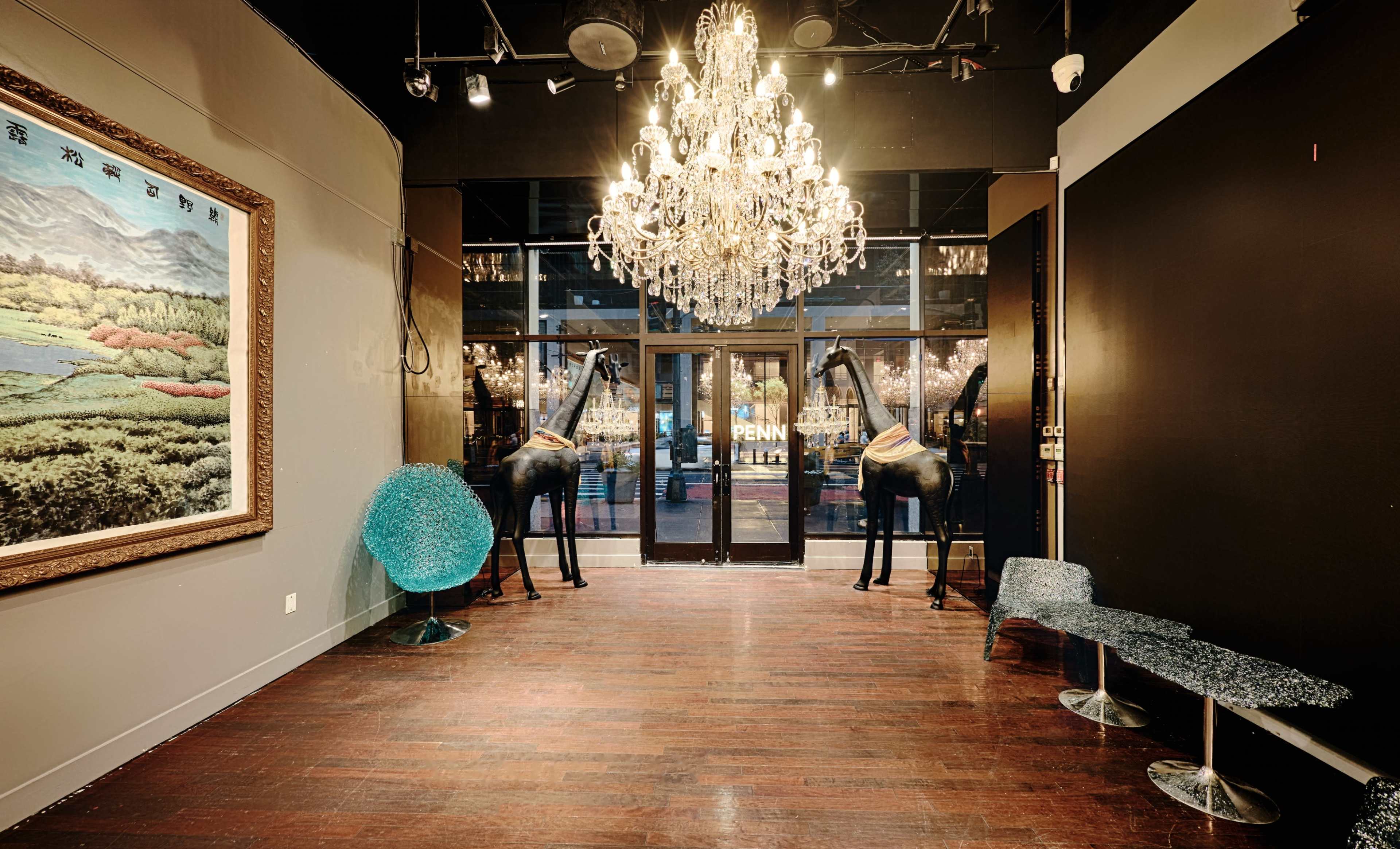The image shows an upscale entrance area featuring a large chandelier, two giraffe sculptures, and a large painting on the wall, all illuminated by soft lighting.