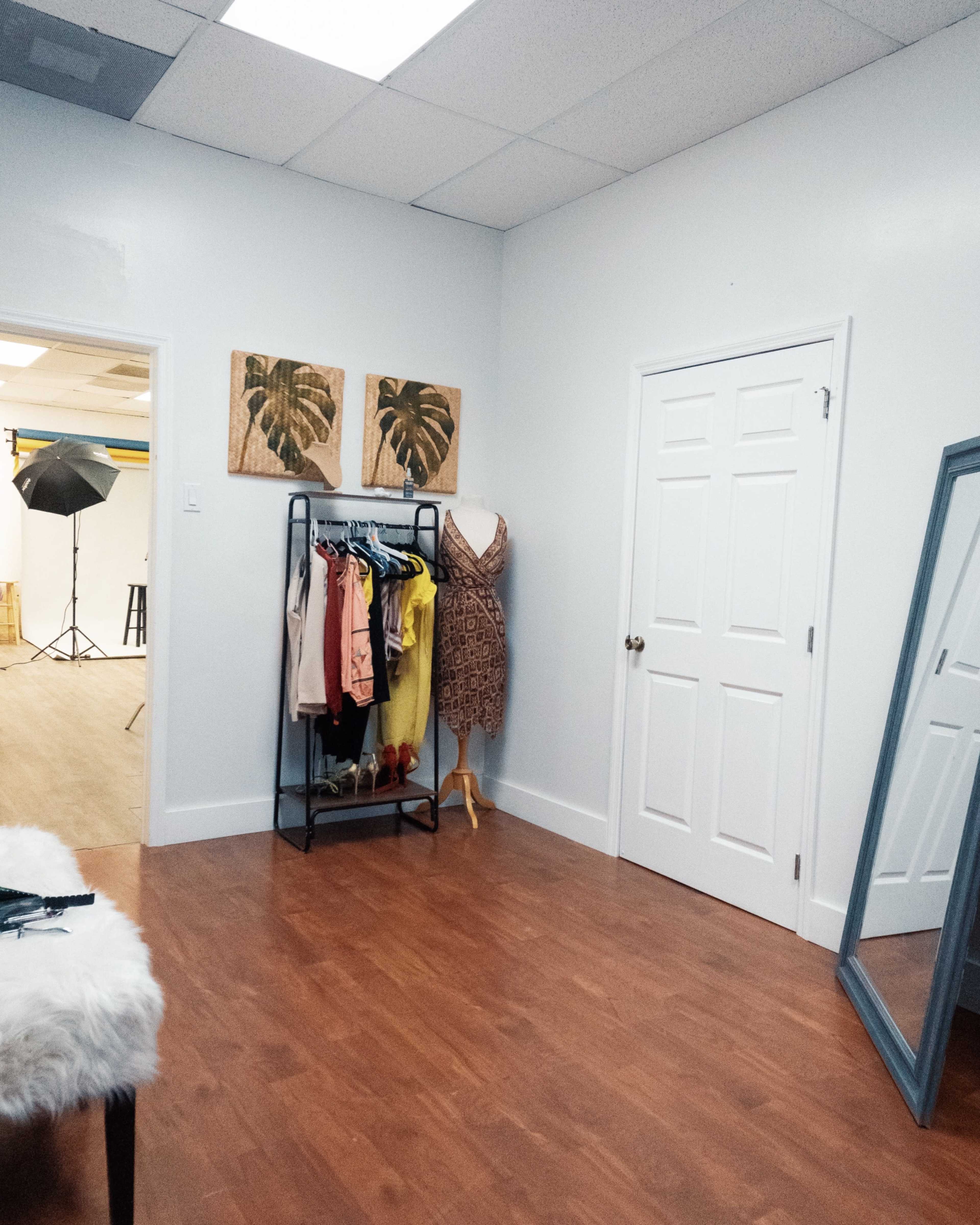 A room with a clothing rack, a dress form, a mirror, and two framed plant prints on the wall.