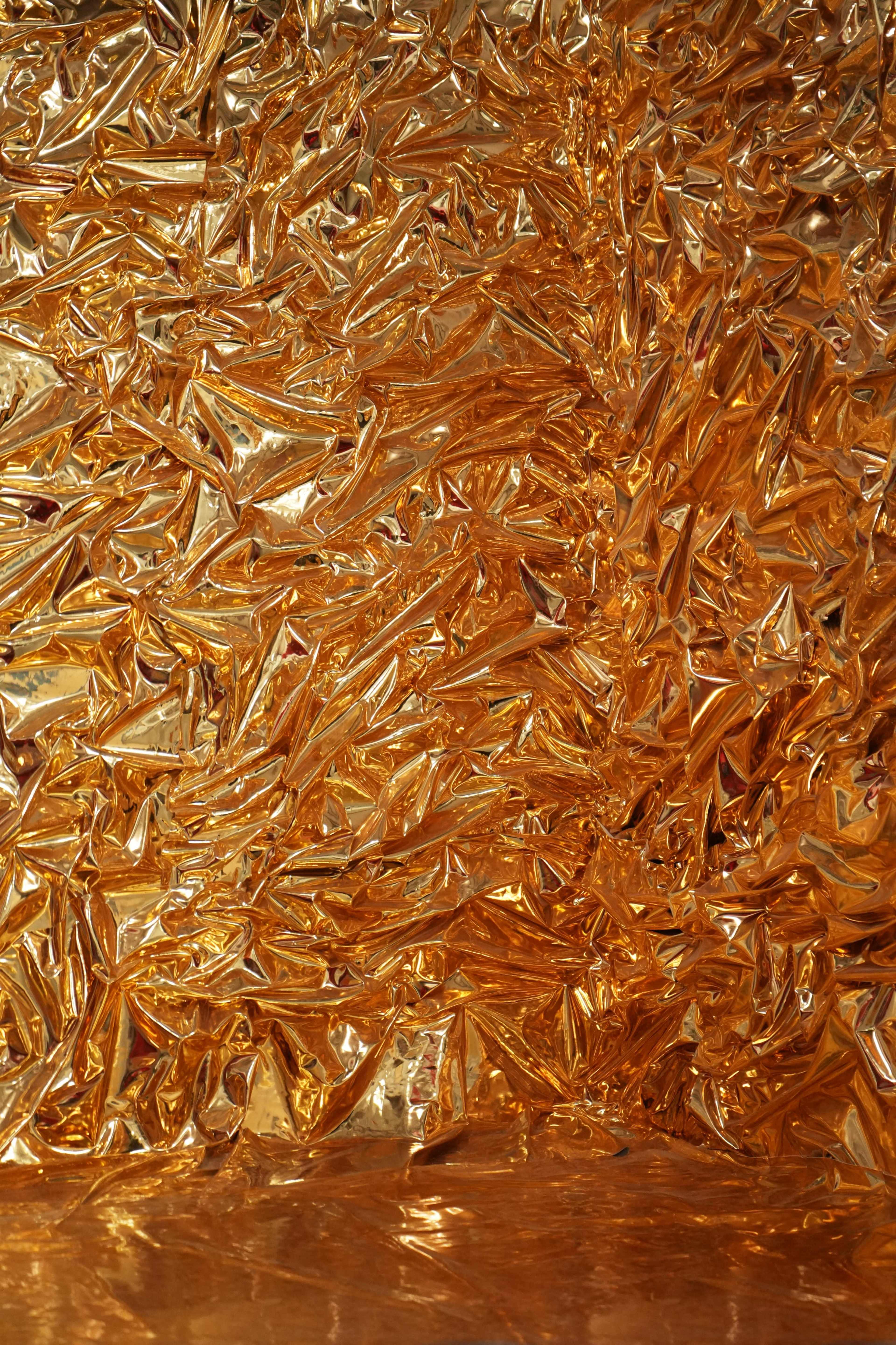 The image features a crinkled, shiny orange foil surface with an abstract texture.