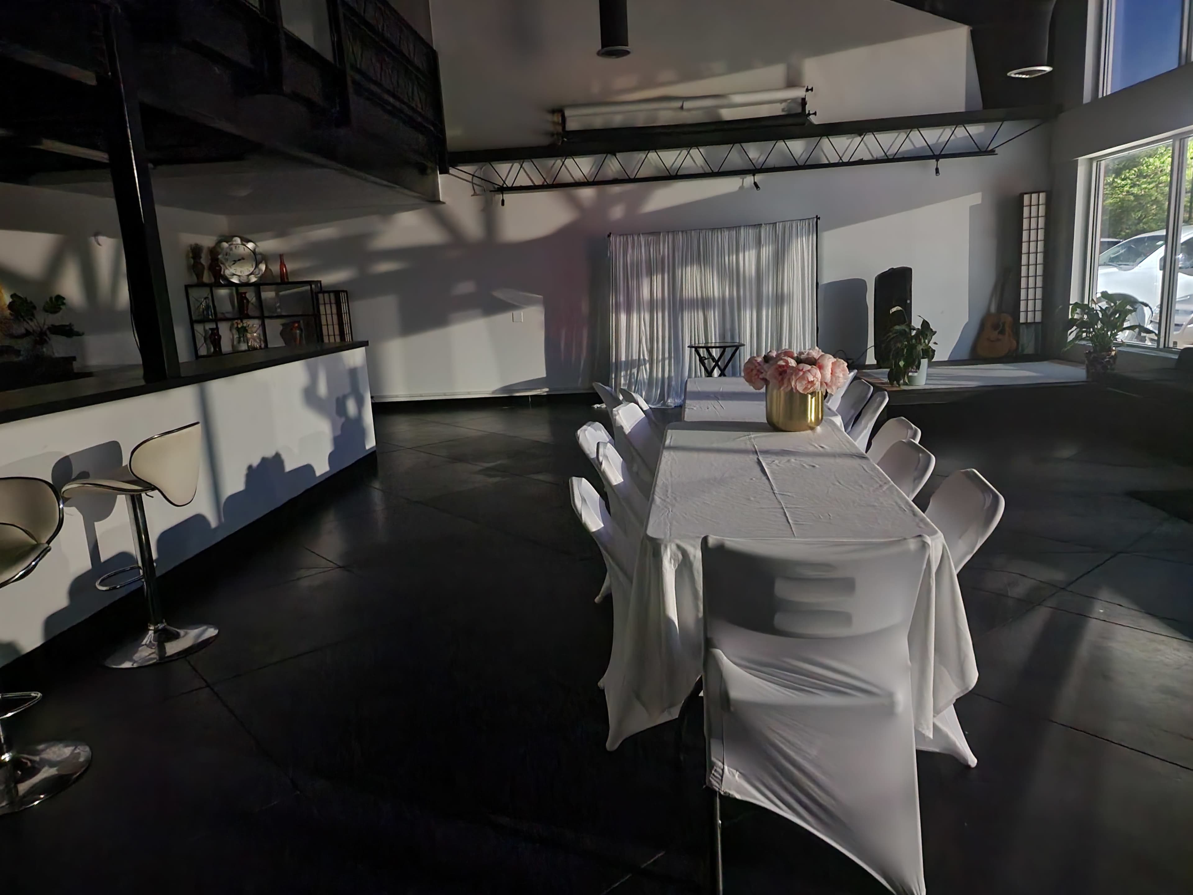 A long table with a white tablecloth is set in a modern, well-lit room featuring a mix of seating and greenery.
