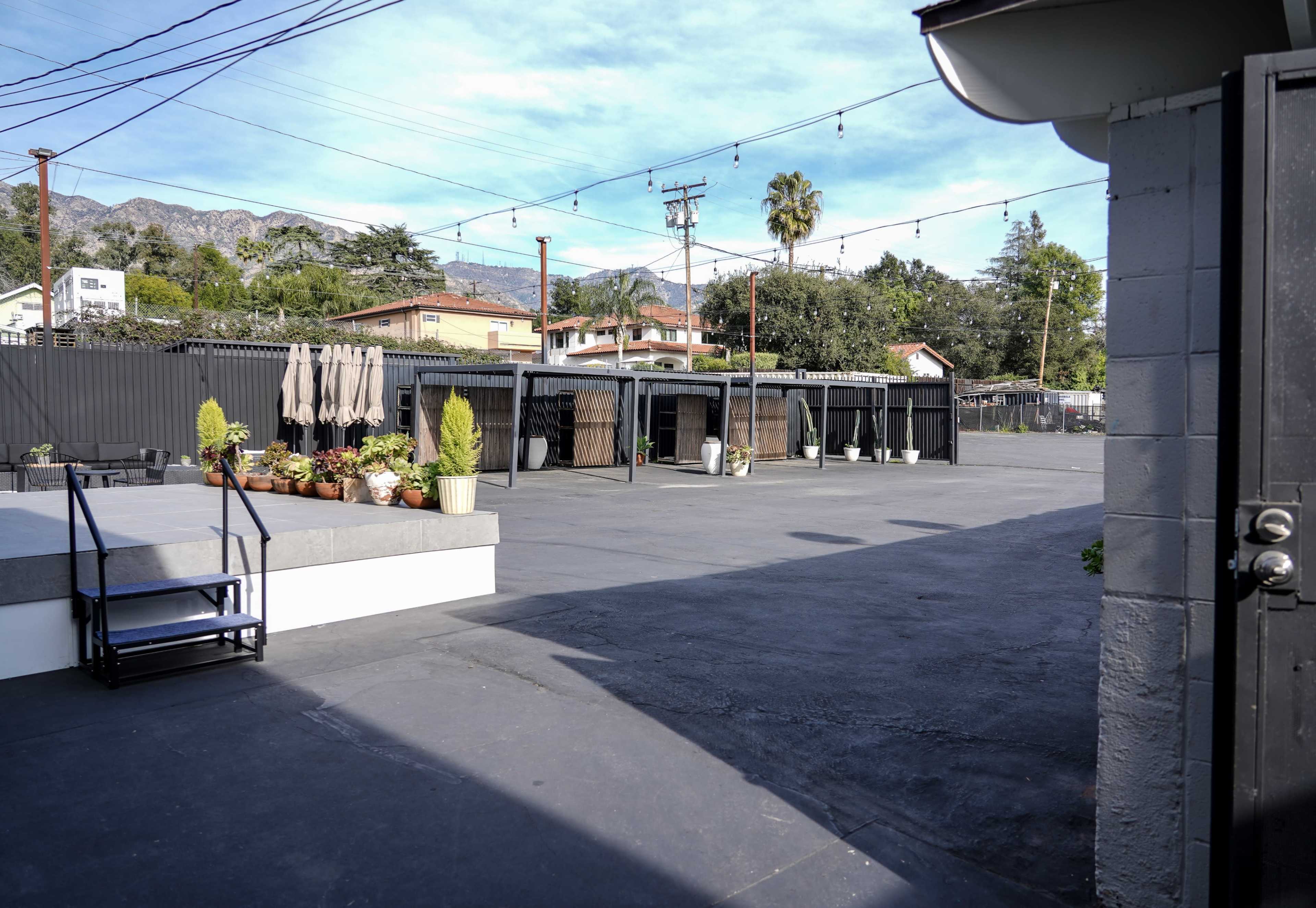 The image shows a spacious outdoor area with several storage units lined along the perimeter and potted plants on a concrete surface under a clear blue sky.