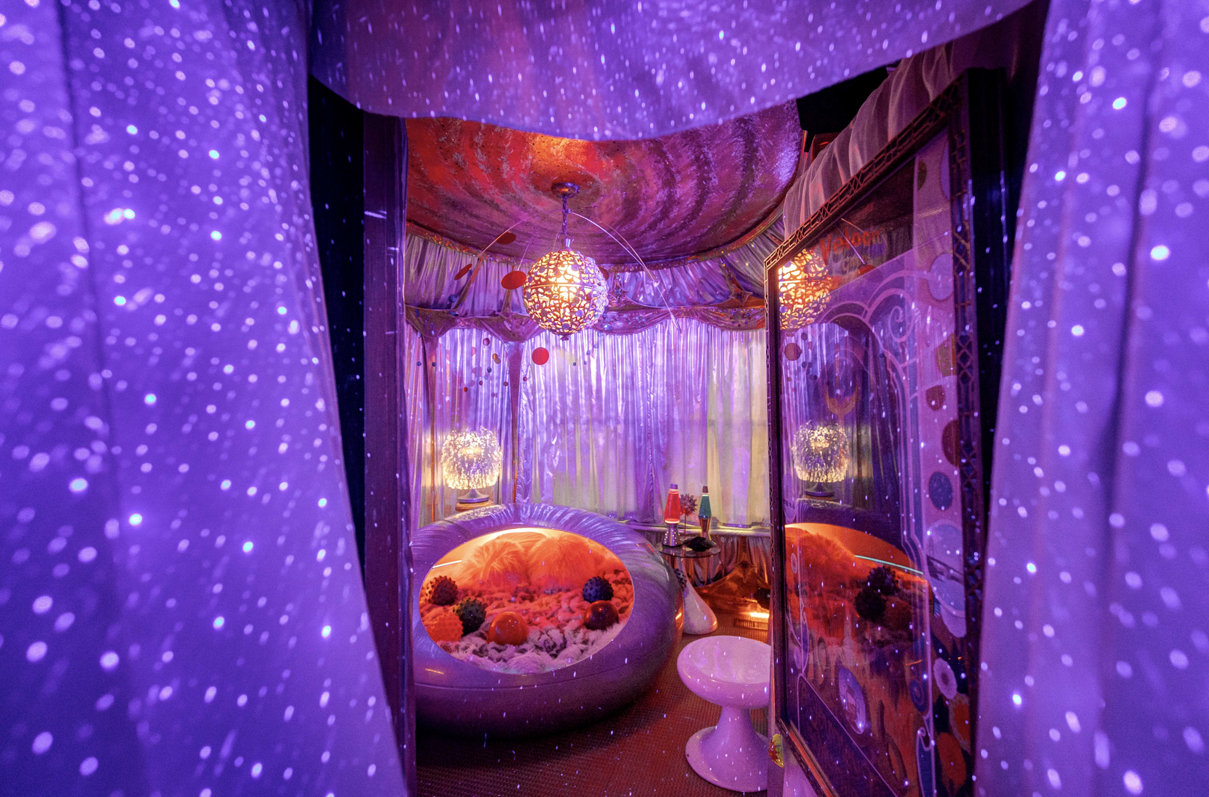 A vibrant, purple-lit room with decorative elements, including a spherical lounge area and shimmering drapes.